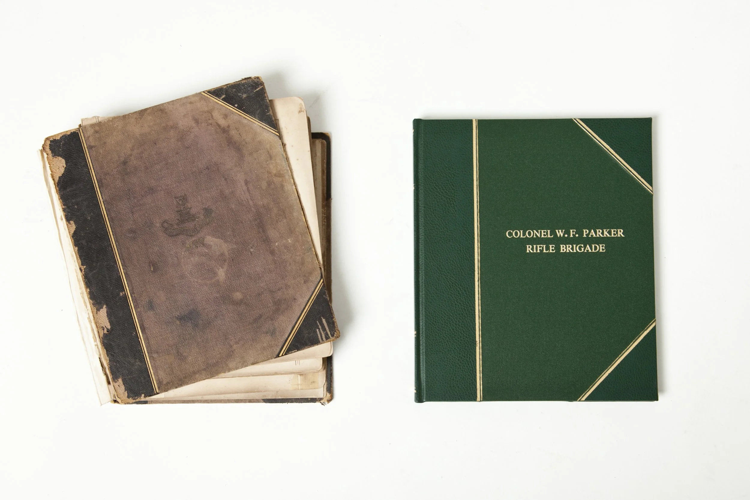 A stack of old, worn books on the left and a new green hardcover book titled 'Colonel W. F. Parker Rifle Brigade' on the right, arranged on a white surface.
