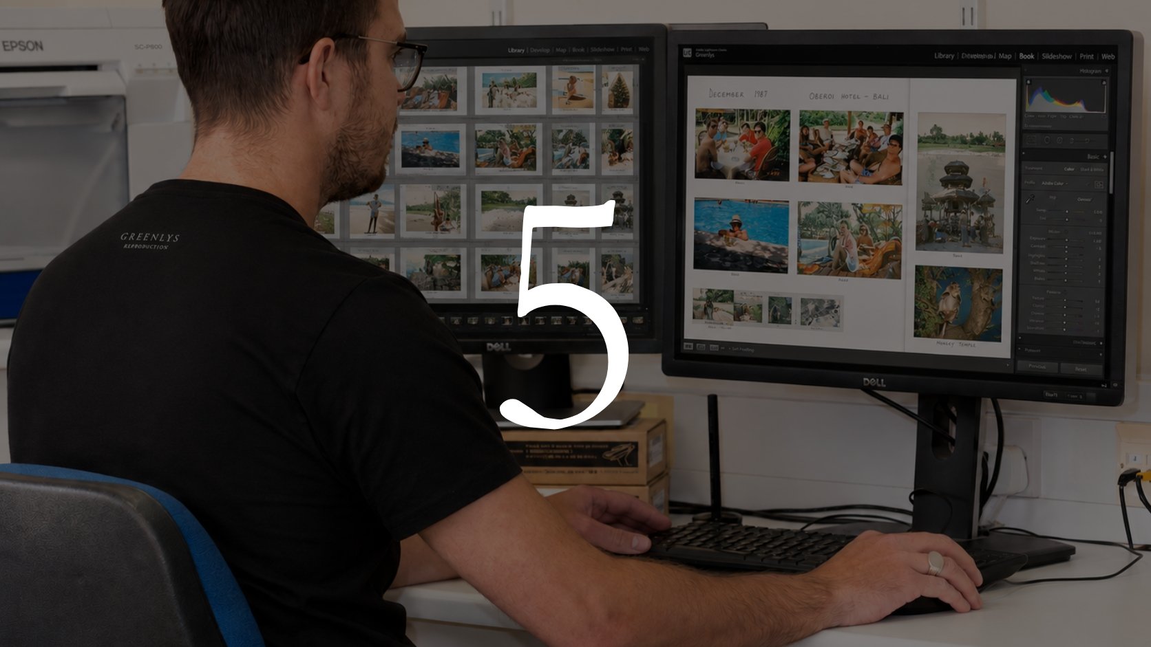 A man with glasses working at a dual monitor computer setup, with photos displayed on both screens, in an office or creative workspace.
