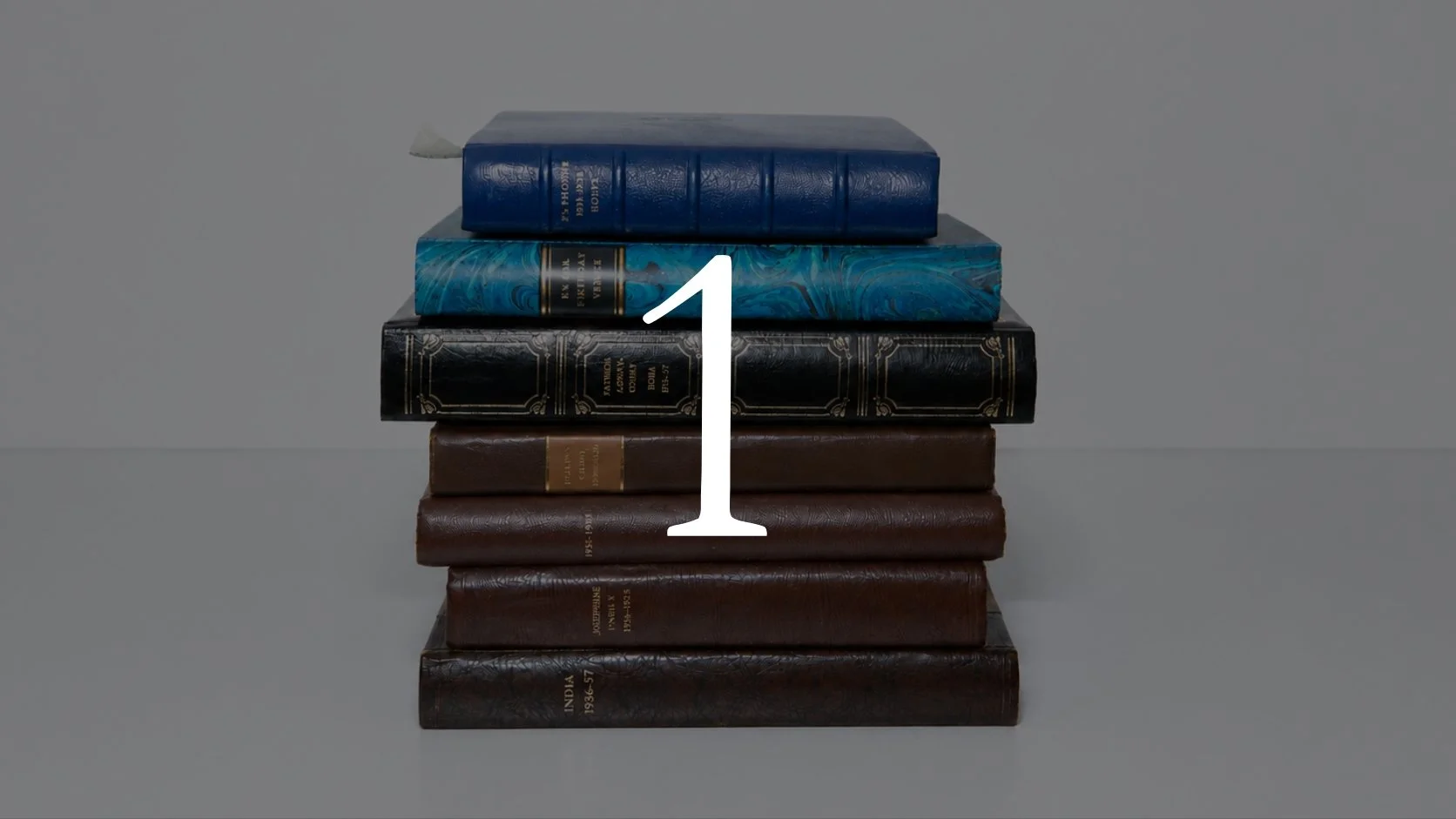 A stack of seven hardcover books arranged on a flat surface against a plain background, with a large white number one overlayed on the image.