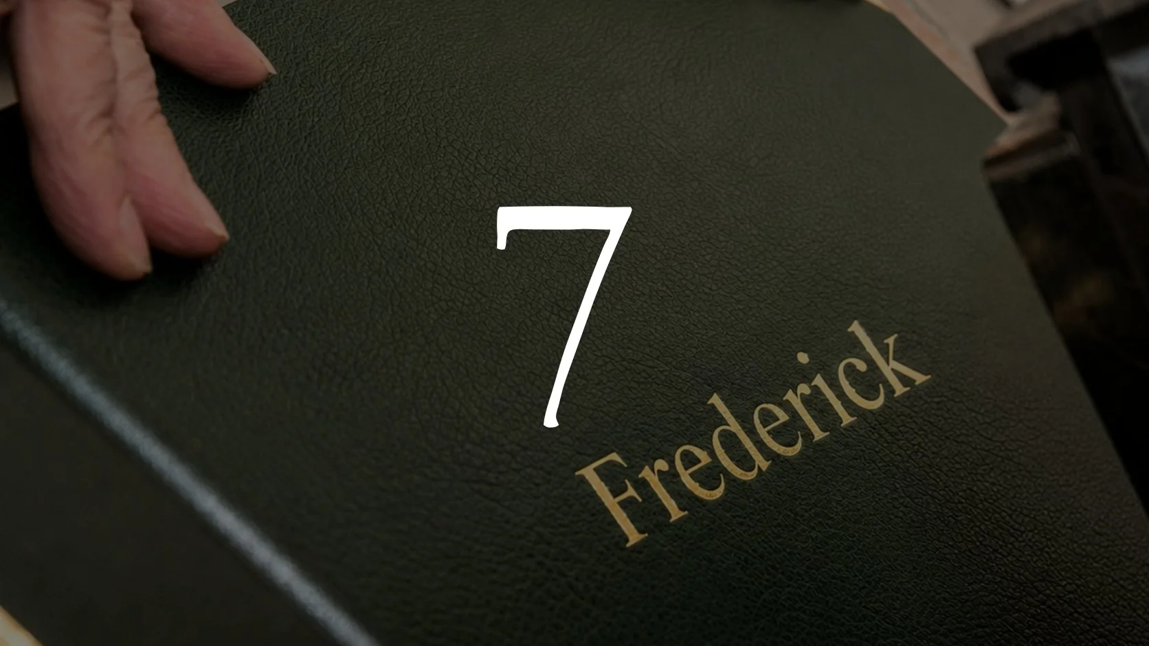 A book or folder labeled with the number 7 and the name Frederick, held by a person's hand.