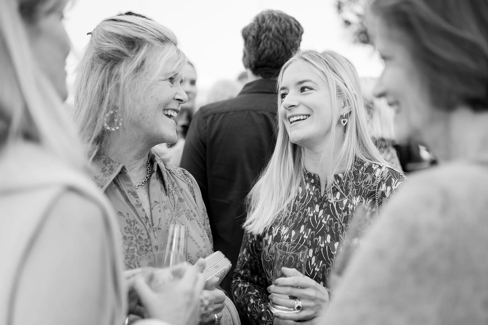 Group of women smiling and chatting at a social event, holding glasses.
