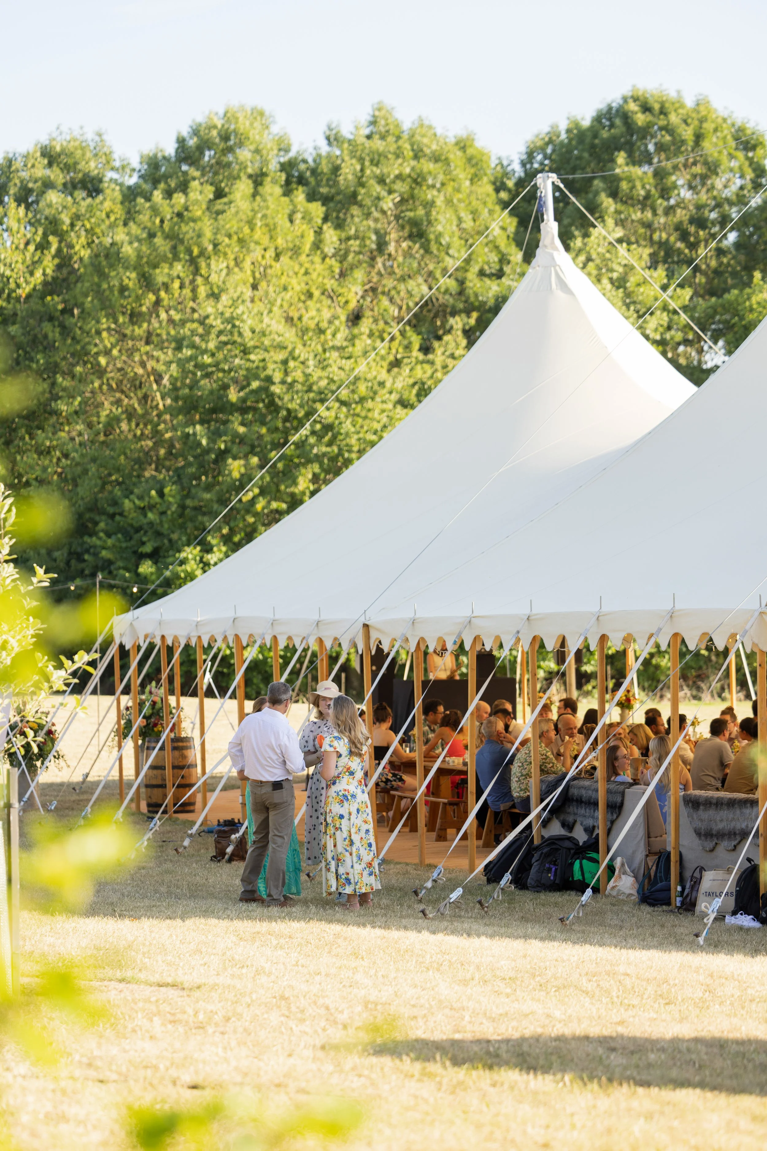 People gathered inside a large white tent at an outdoor event, with trees in the background.