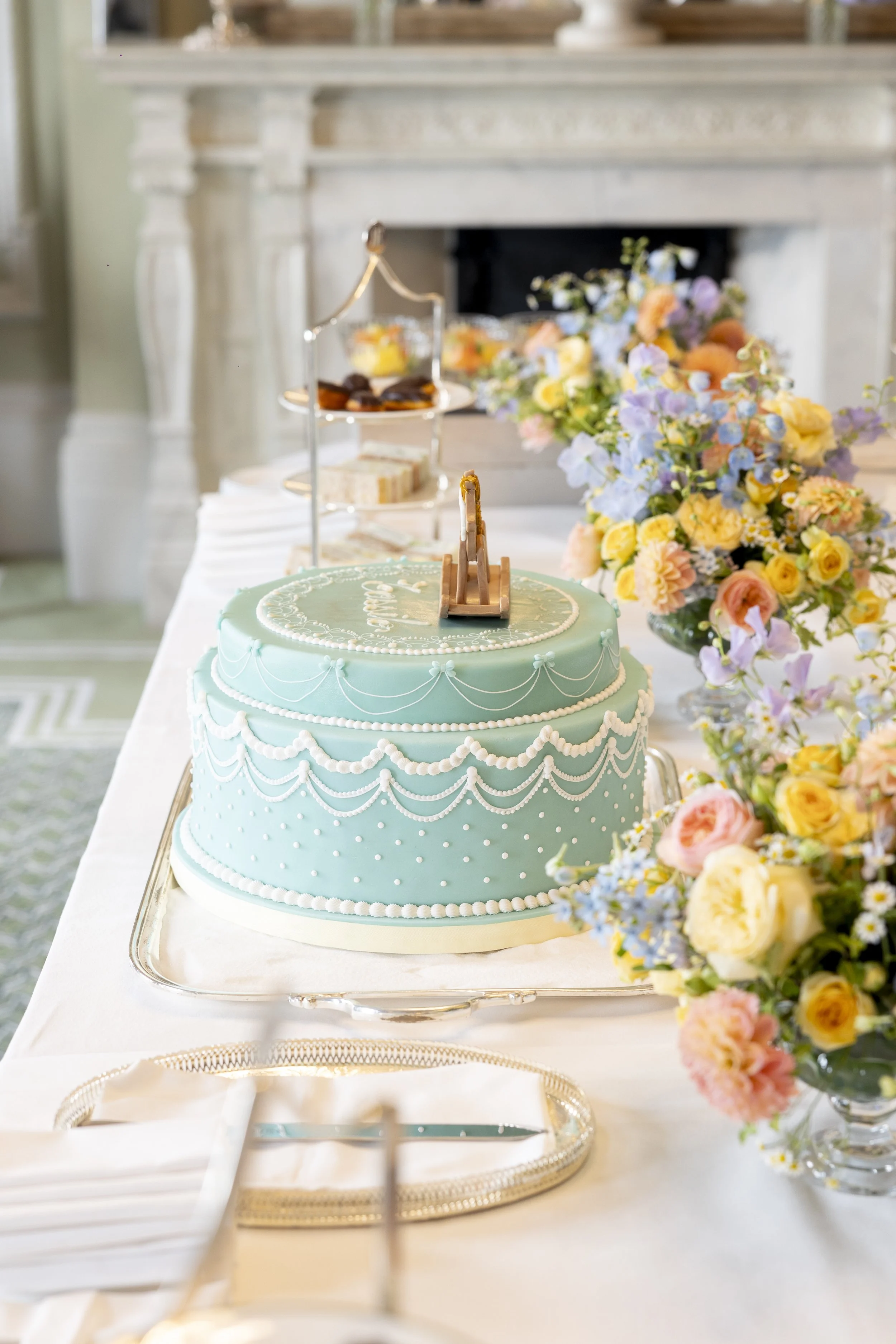 A pastel blue wedding cake with white decorative piping and pearl-like accents, placed on a silver tray on a decorated table with colorful flowers in vases.