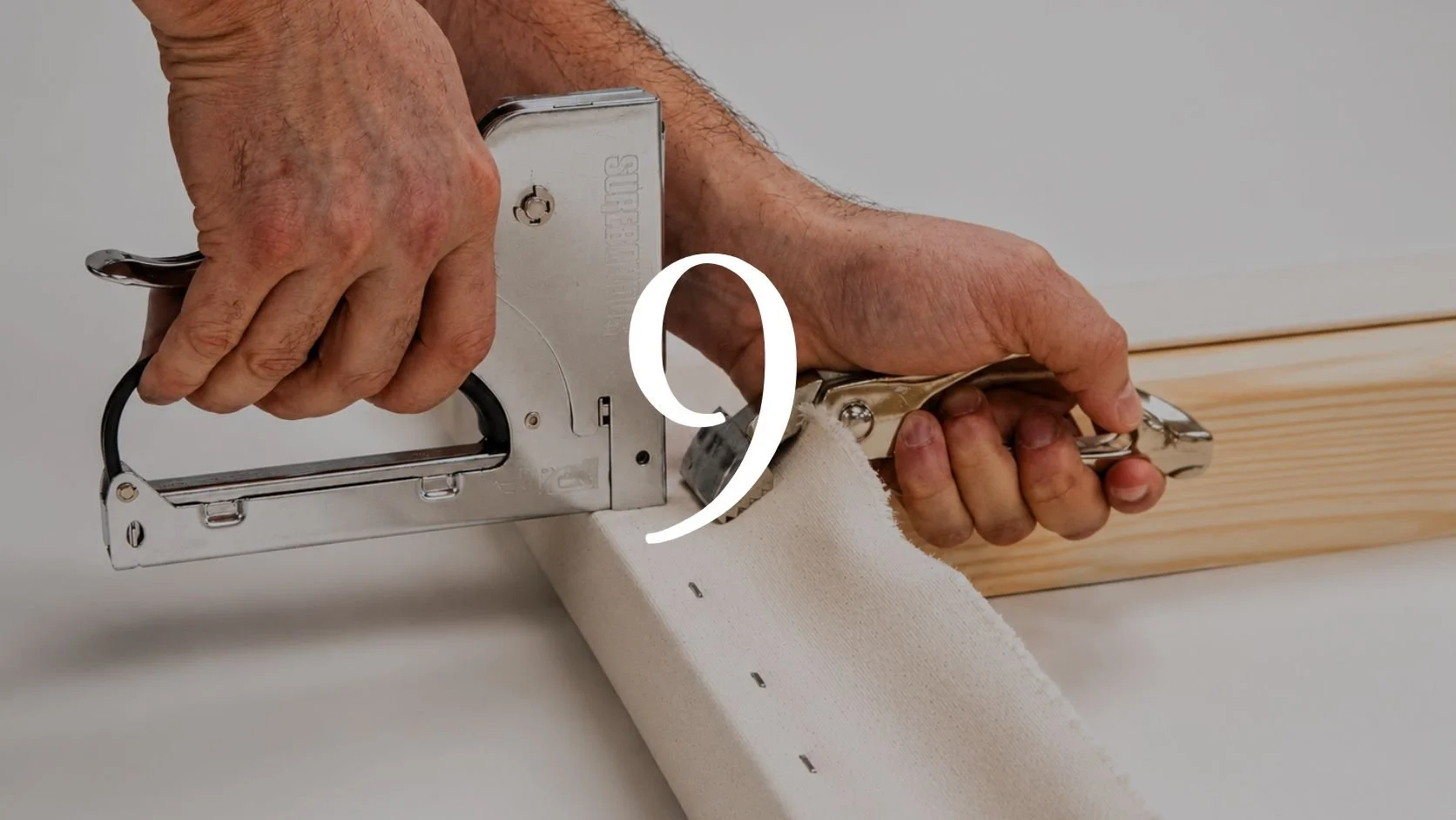 A person using a staple gun to attach fabric to a wooden surface.