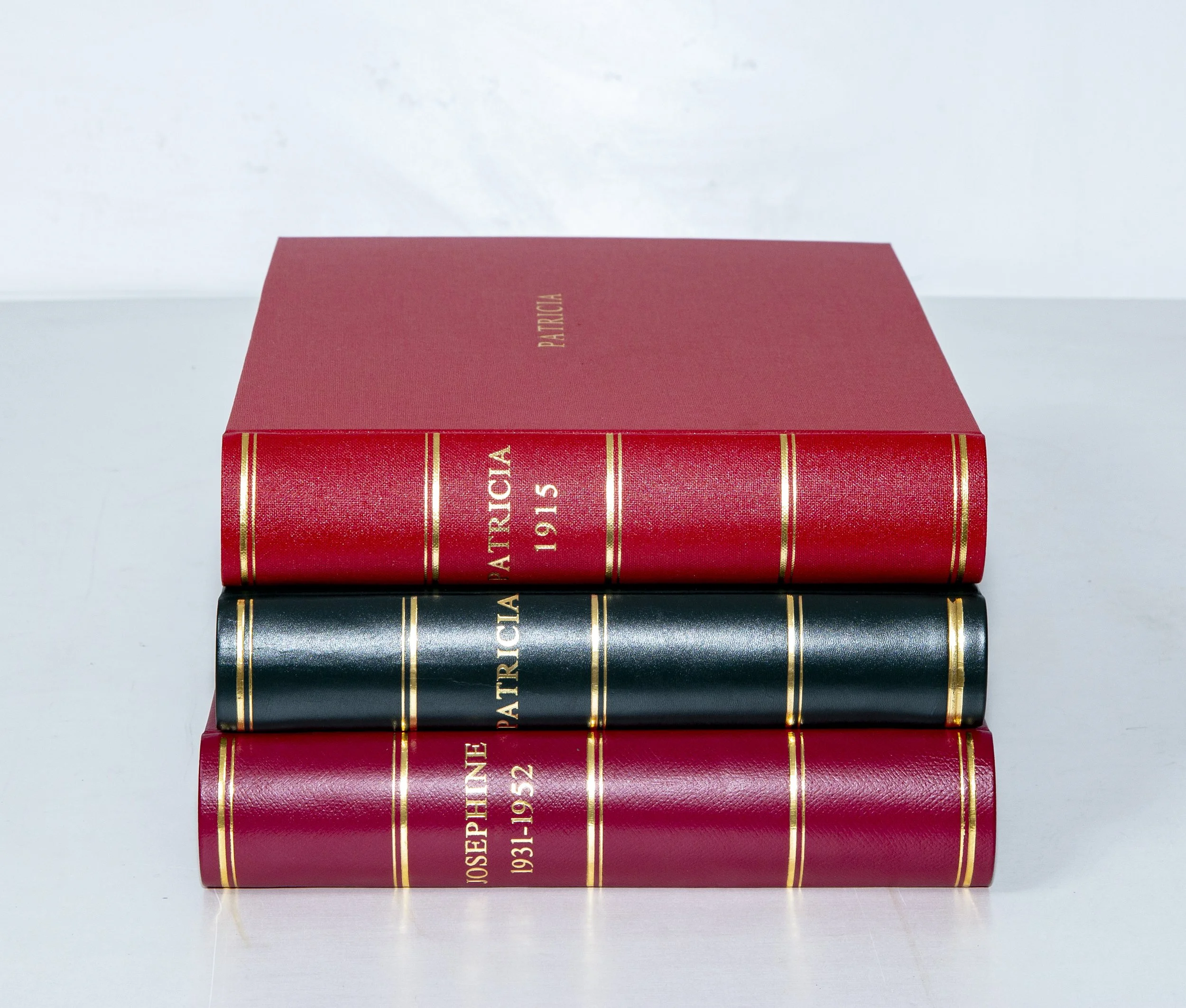 Three hardcover books stacked on a white surface with a red box on top. The books are titled about Patricia and Josephine, with gold lettering on the spines.