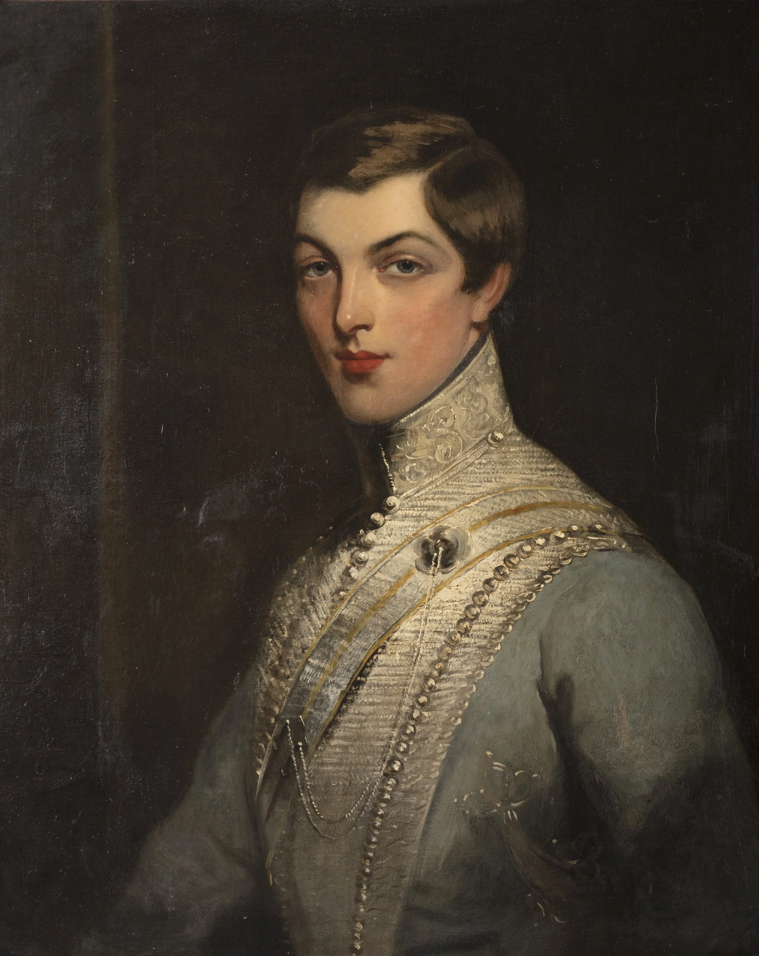 Portrait of a woman with light skin, short brown hair, and blue eyes. She wears a high-collared, ornate dress with beads and embroidery.