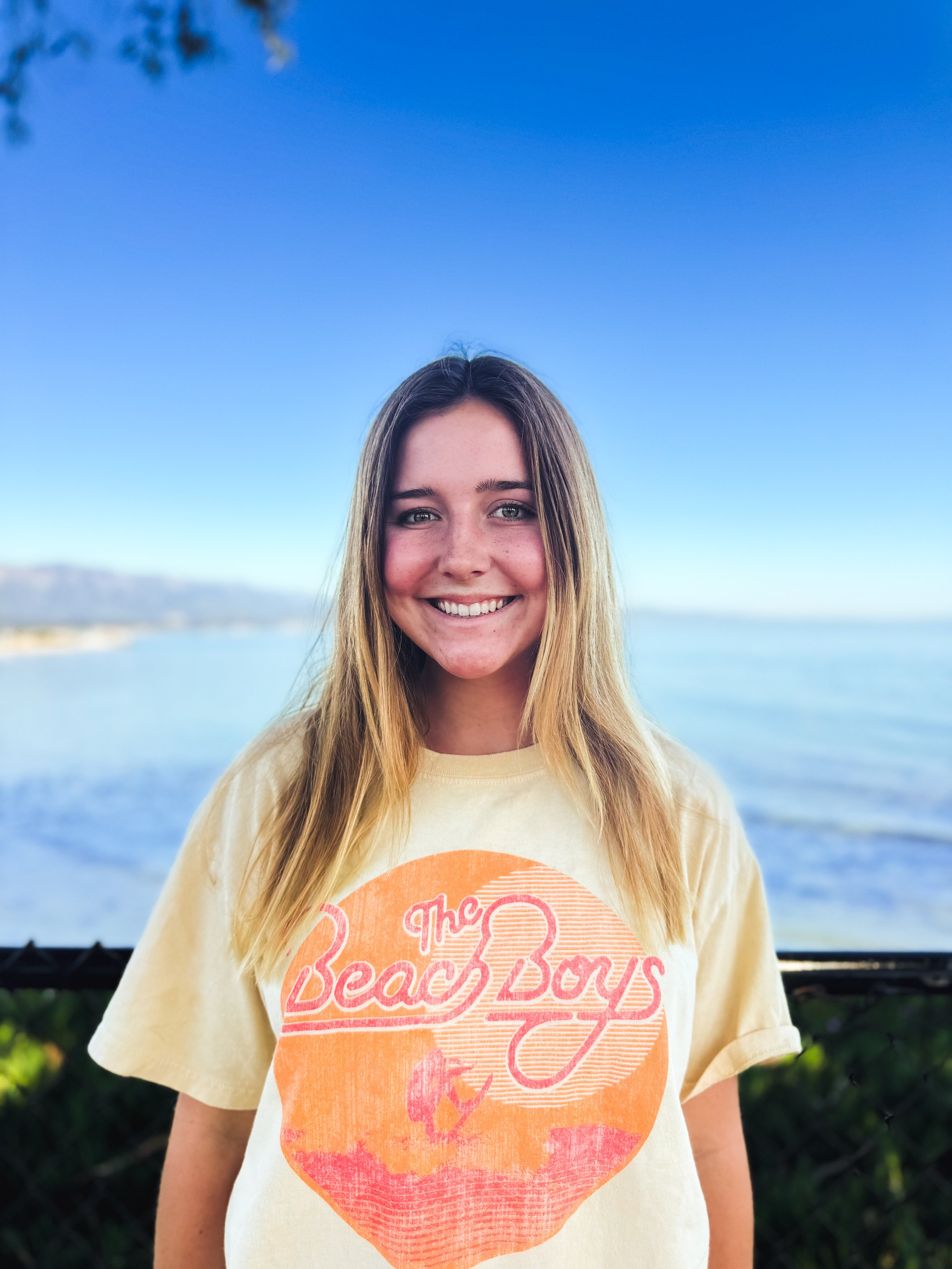Person smiling in a "The Beach Boys" T-shirt with ocean background