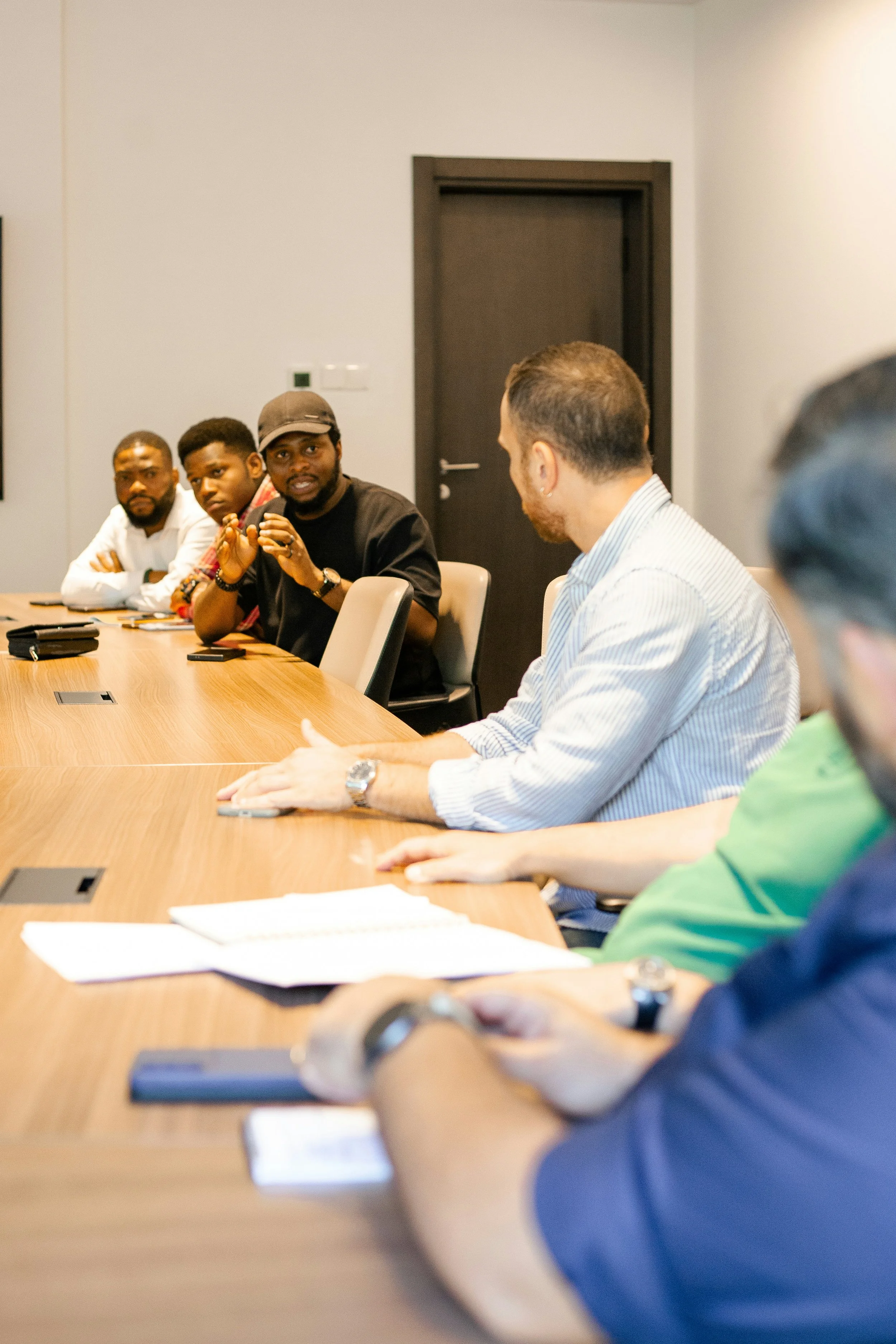 A diverse group of people sitting around a conference table in a meeting, with one man speaking and others listening attentively.