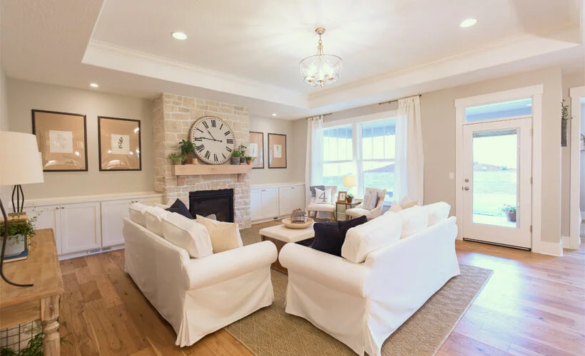 A neutral living room with white Ikea Ektorp sofas, warm gray walls, a beige stone fireplace and a tray ceiling.