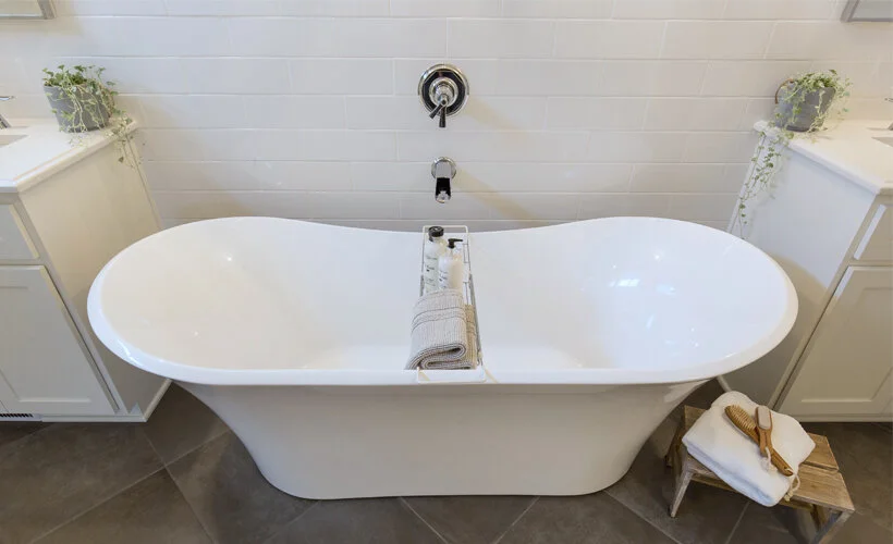 A free standing tub with a wall mounted Brizo tub filler and white subway tile wainscoting.