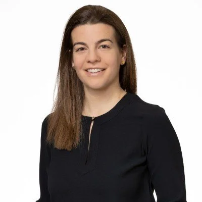A woman with brown hair, wearing a black top, smiling against a white background.