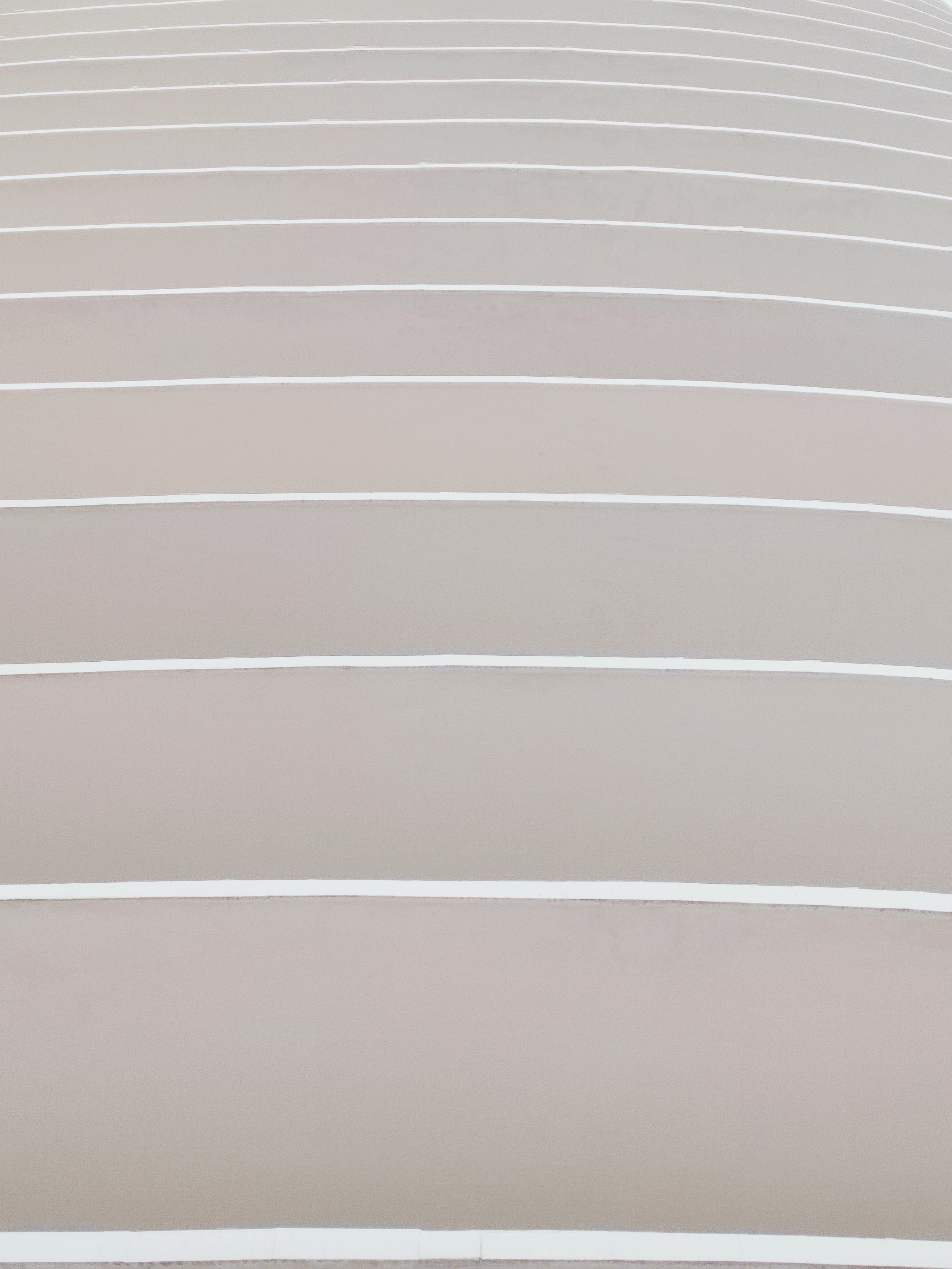 Close-up of a modern, beige exterior wall with horizontal white lines and curved architectural design.