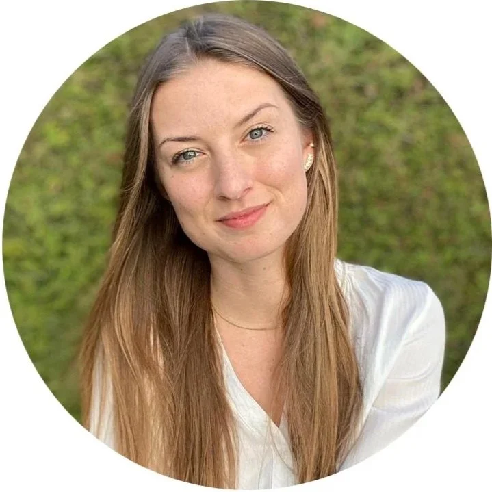 Headshot of a woman with long light brown hair, wearing a white shirt, smiling, outdoors with a green background.