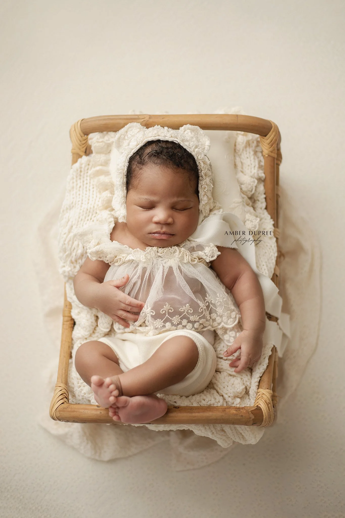 newborn baby in a lace bear bonnet and white outfit