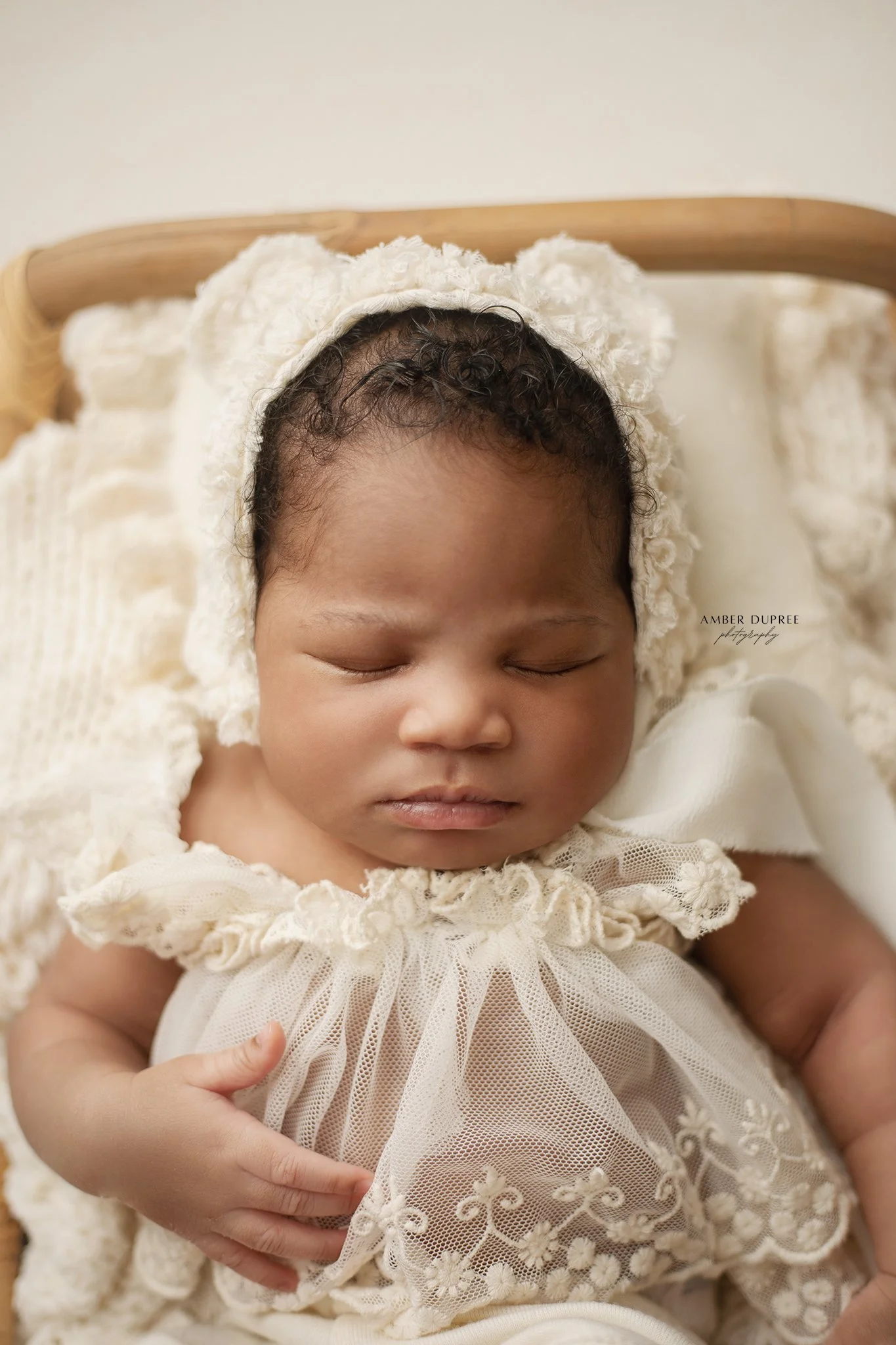 close up newborn baby in a lace bear bonnet and white outfit