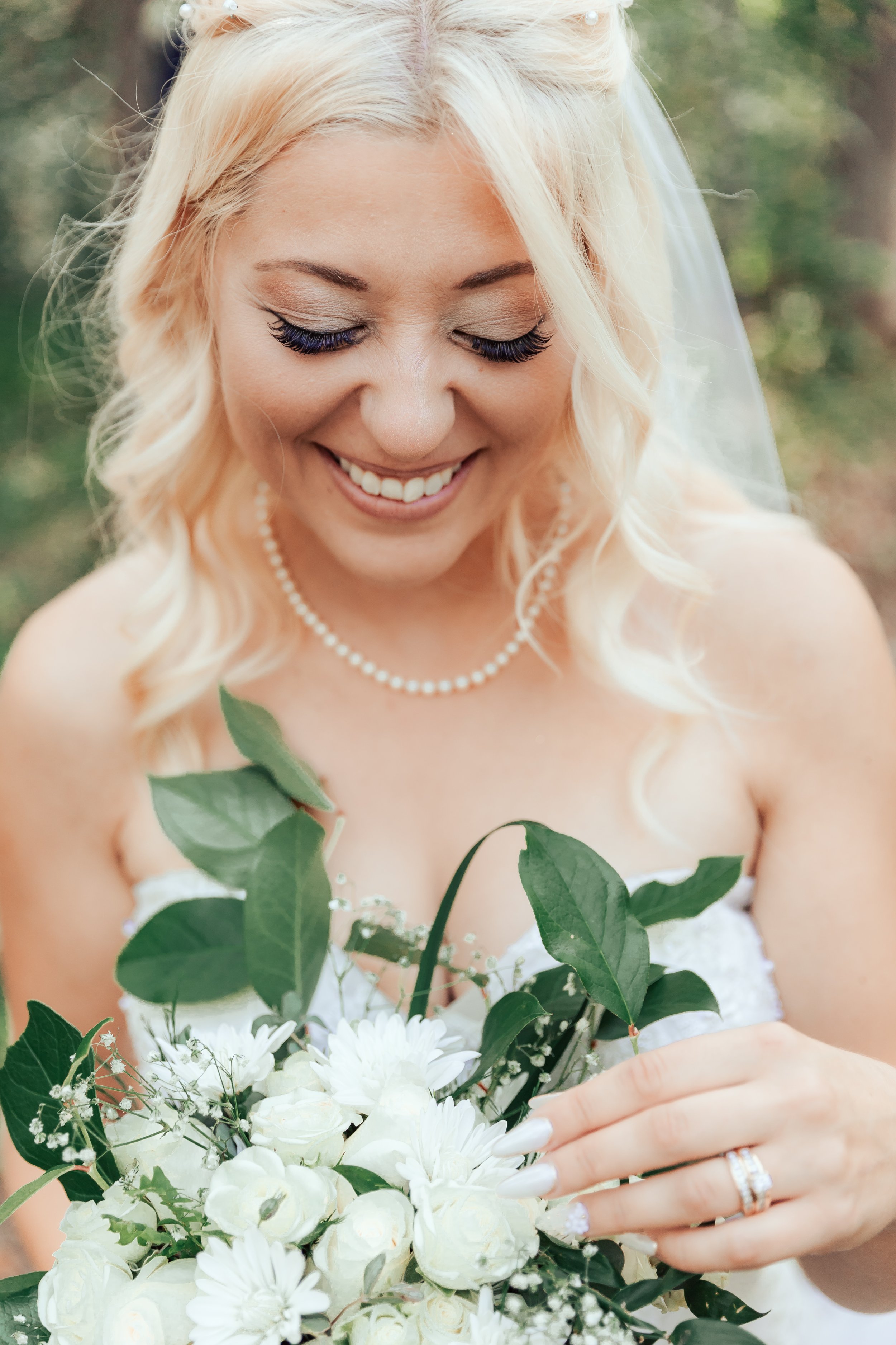 Smiling bride with bouquet of white roses and greenery.