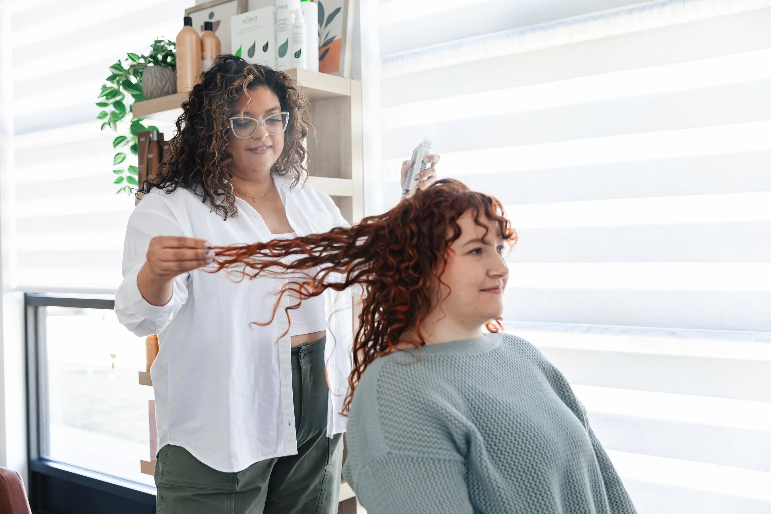 Hairdresser beim Styling rotbrauner, lockiger Haare einer Kundin in einem Friseursalon
