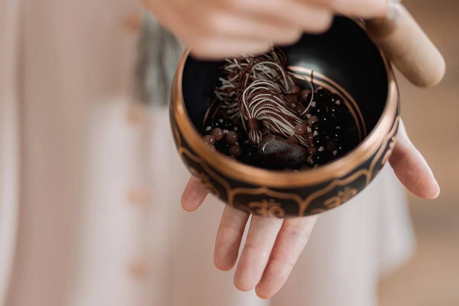 Person holding a singing bowl containing beads and a tassel.