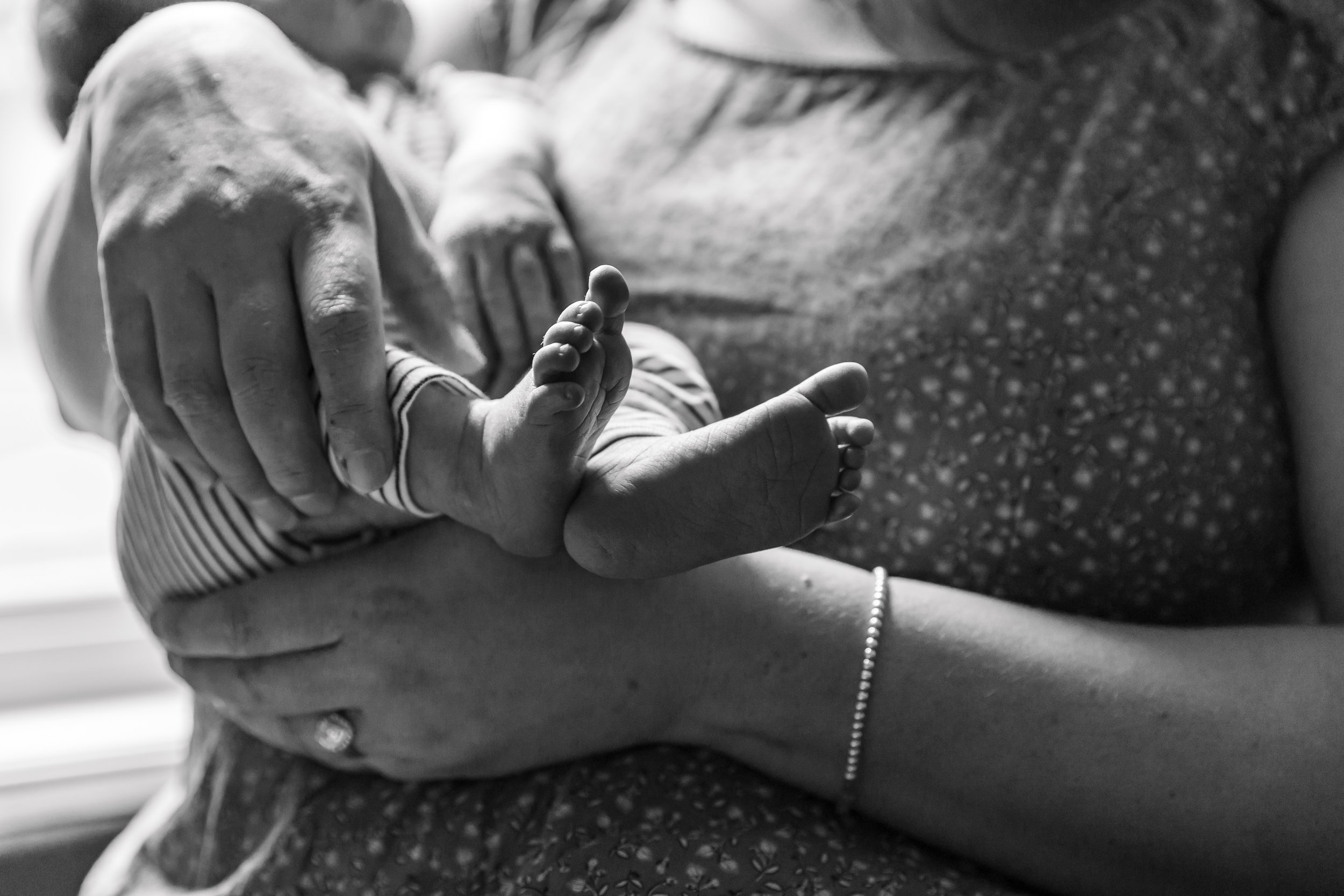 Black and white photo of a baby being held, focusing on the baby's feet and an adult's hands in the background.