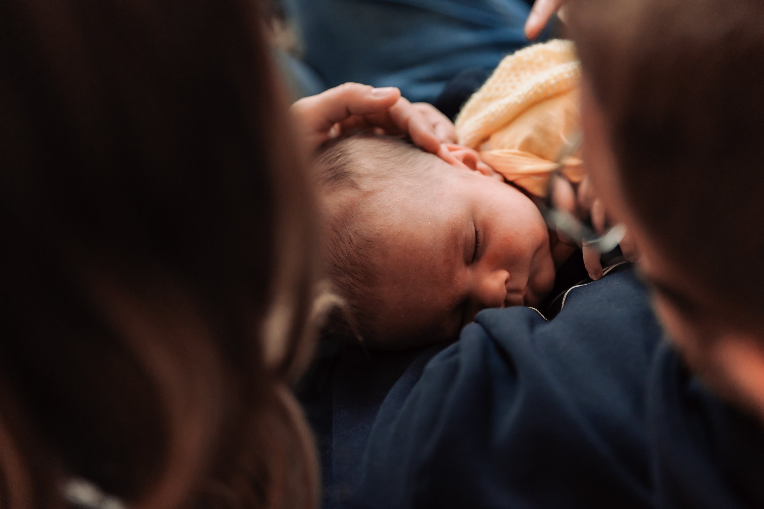 A baby sleeping peacefully on an adult's chest, with an adult's hand gently cradling the baby's head.