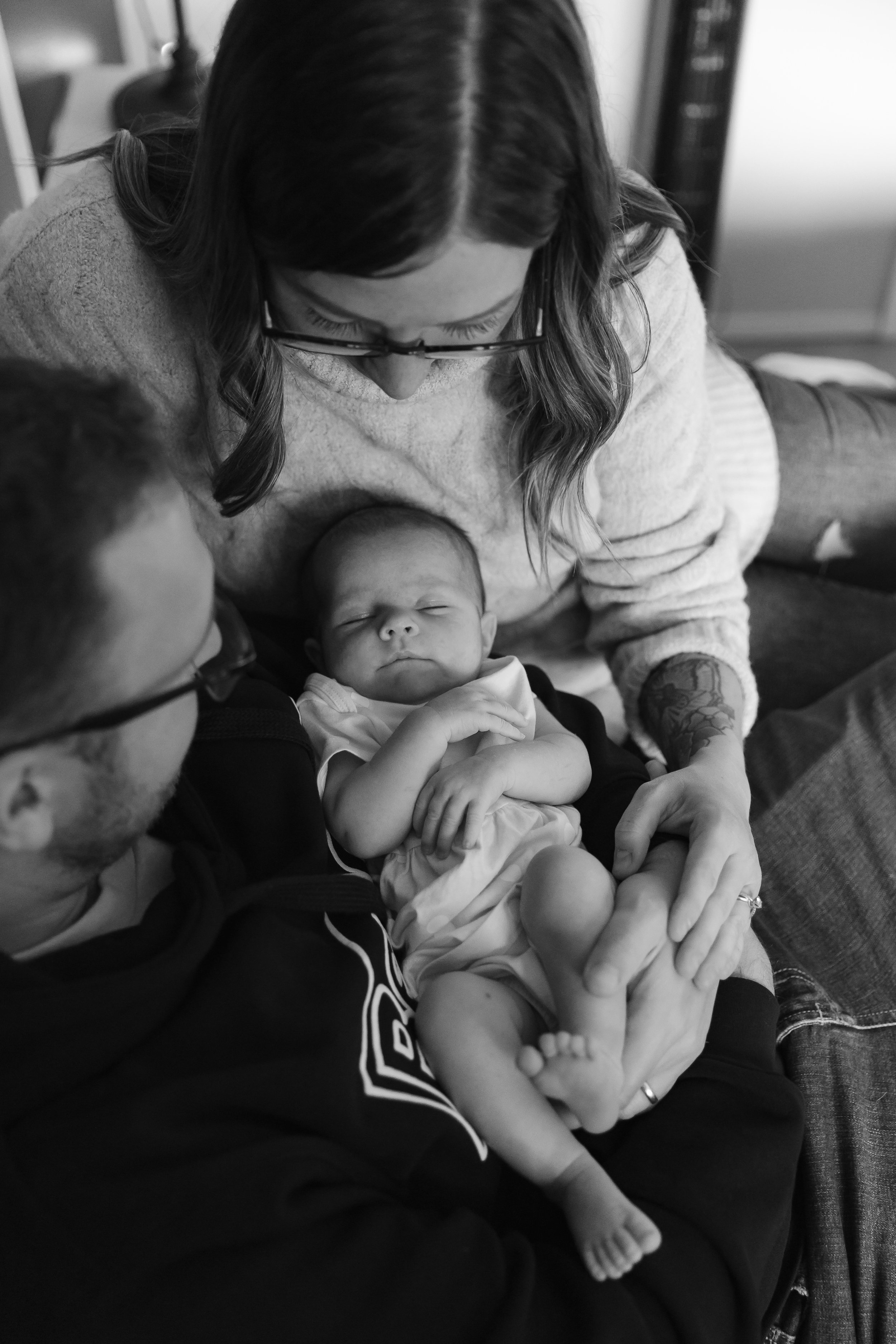 A black and white photo of a couple holding a sleeping baby, with the woman's head bent down affectionately towards the child.
