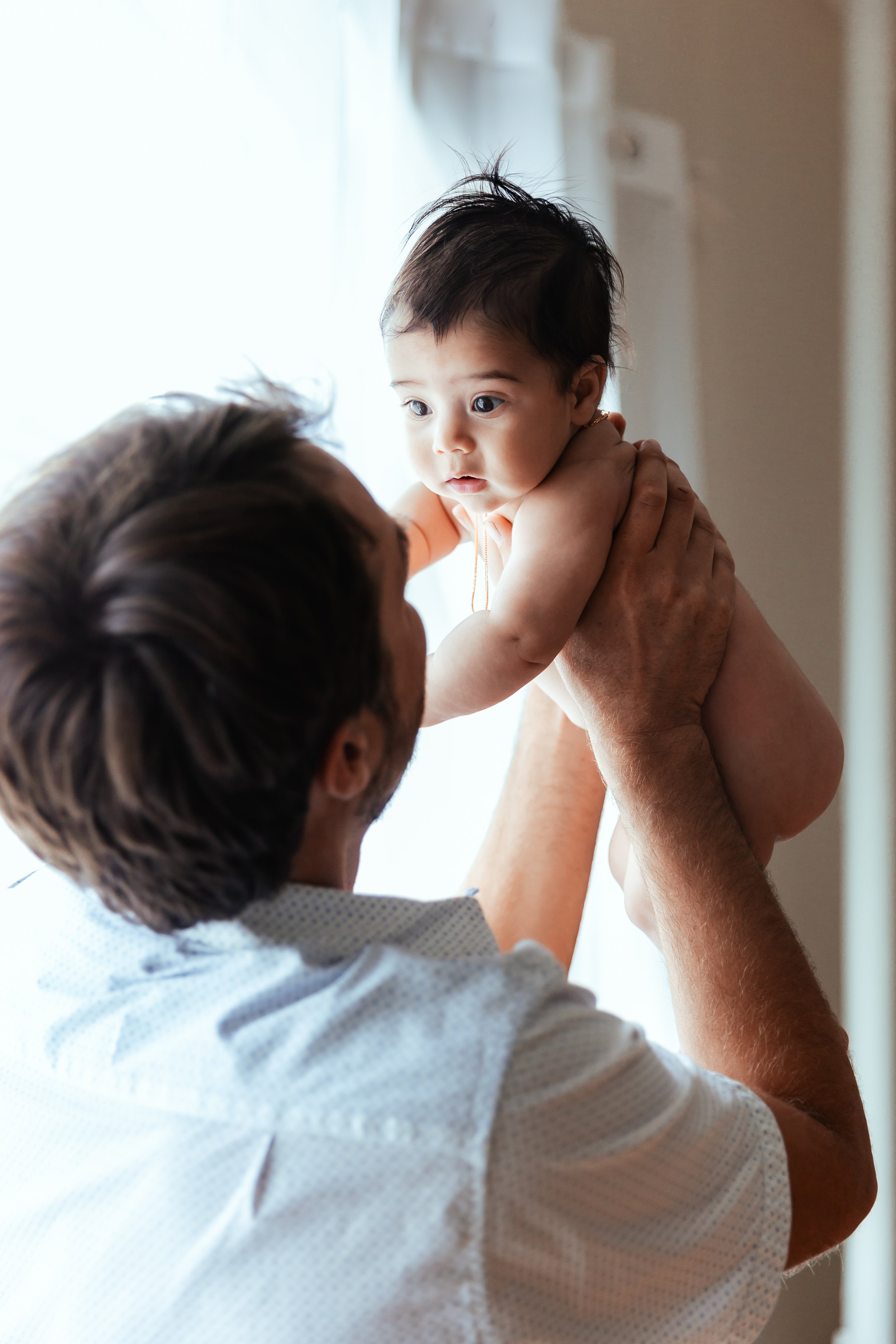 Man holding a baby near a window, looking at each other.
