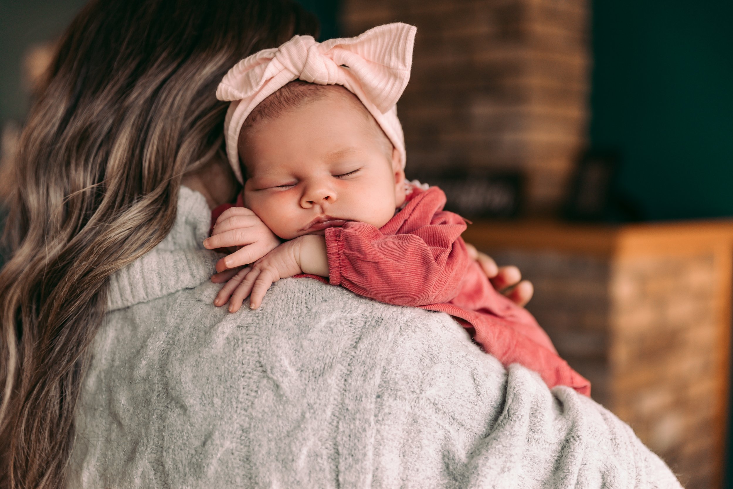 Sleeping baby with pink headband on person's shoulder.
