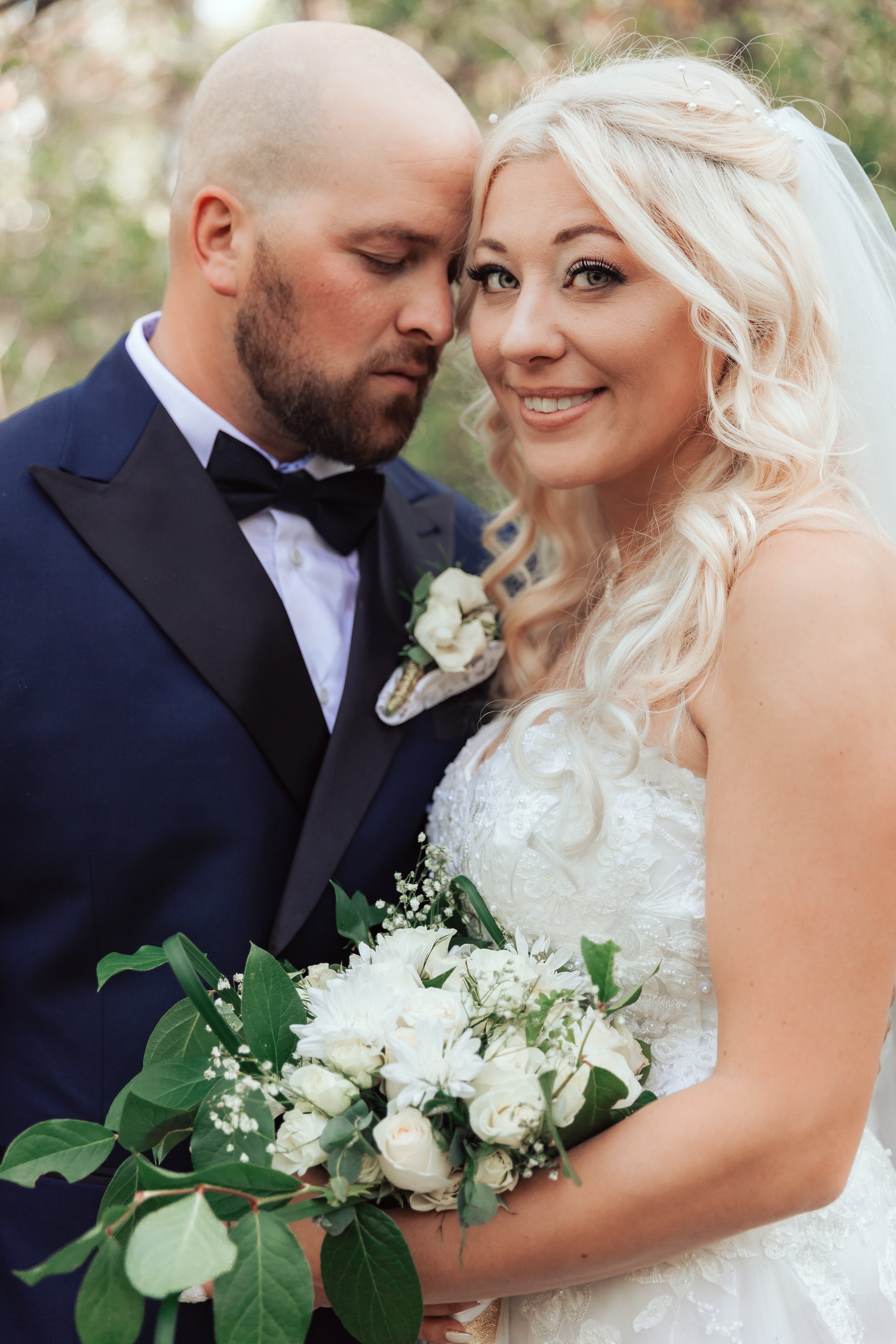 Bride and groom embracing with bouquet of white flowers.