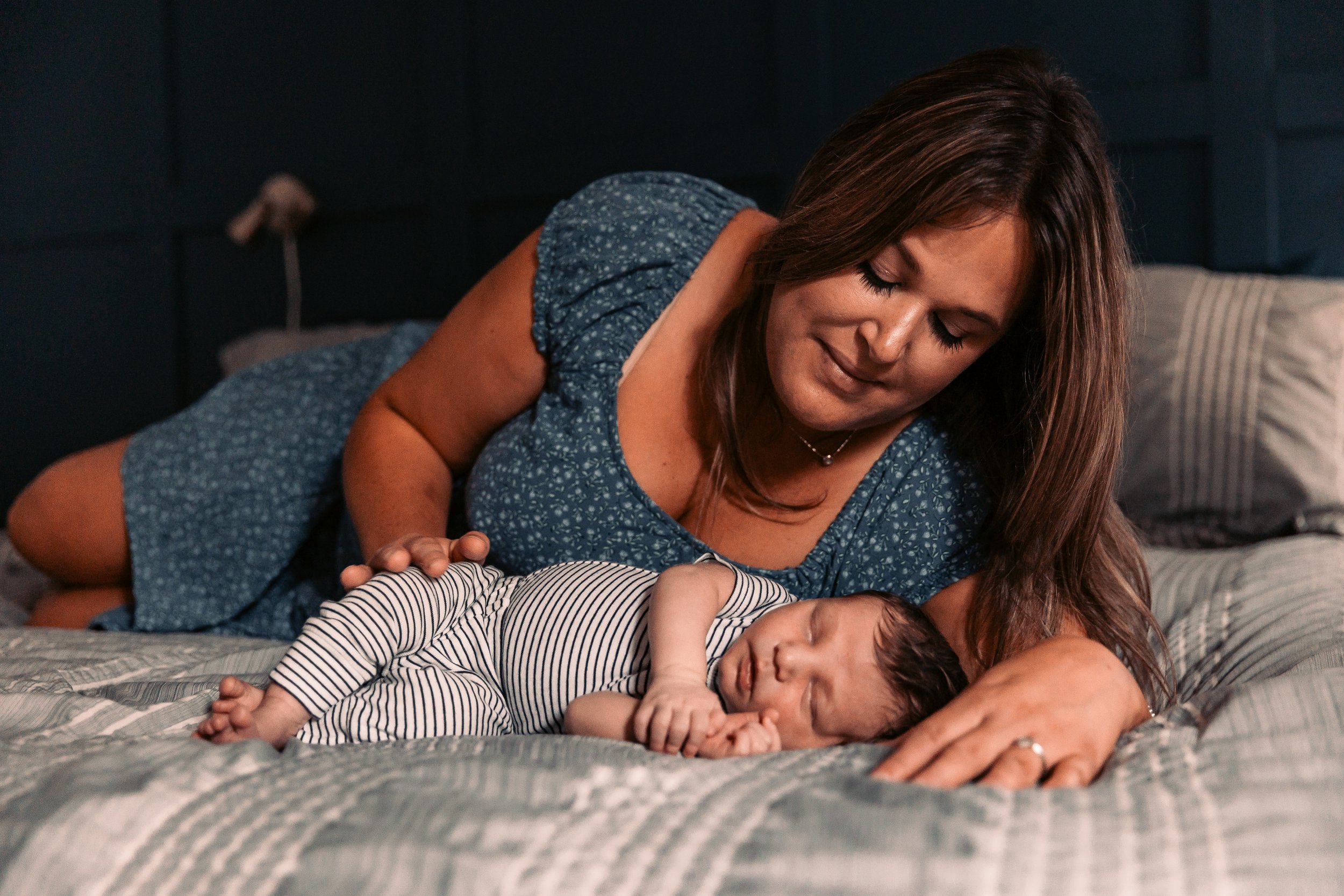 A woman lying on a bed next to a sleeping baby wearing striped pajamas.