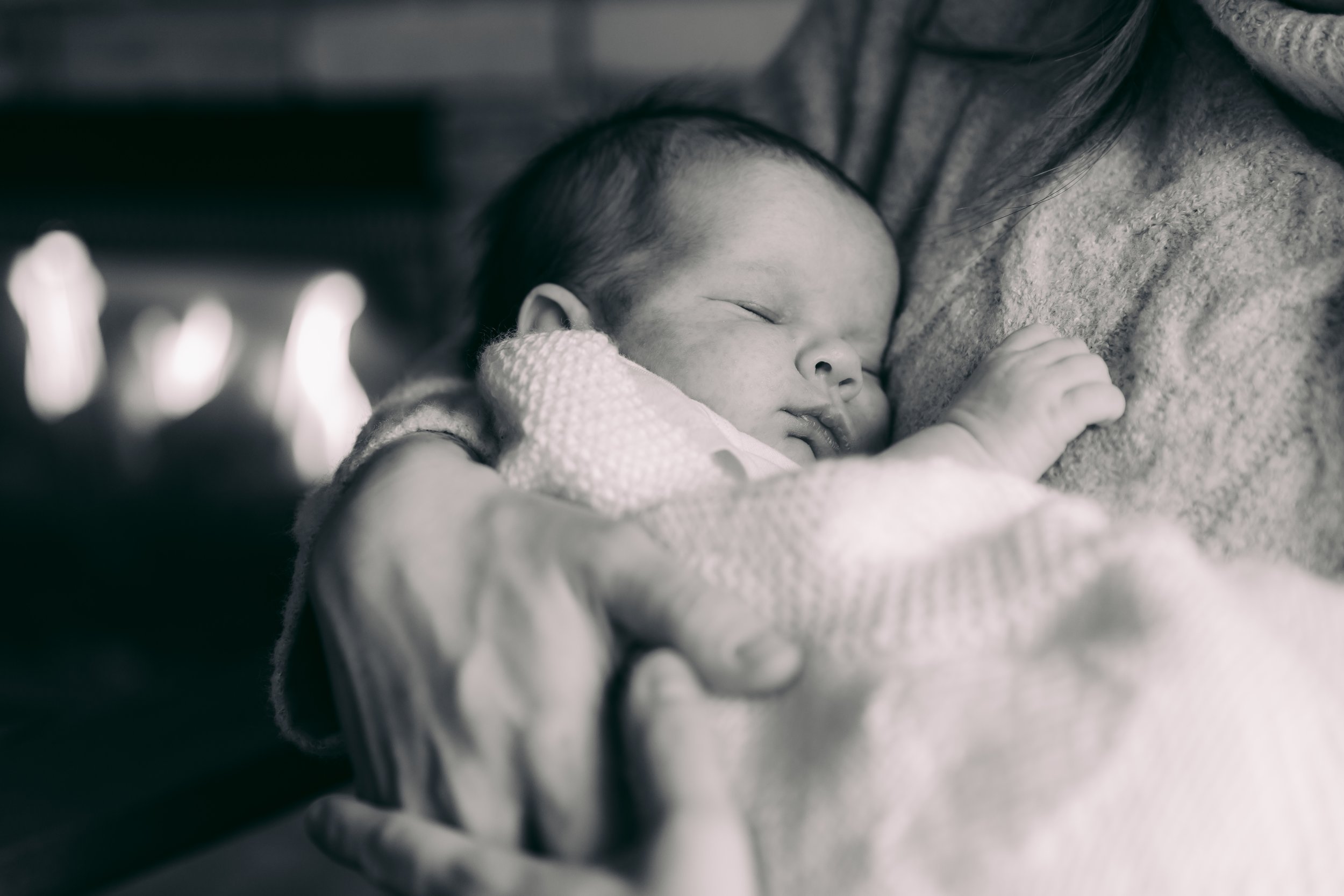 Black and white photo of a sleeping baby wrapped in a blanket, cradled in an adult's arms.