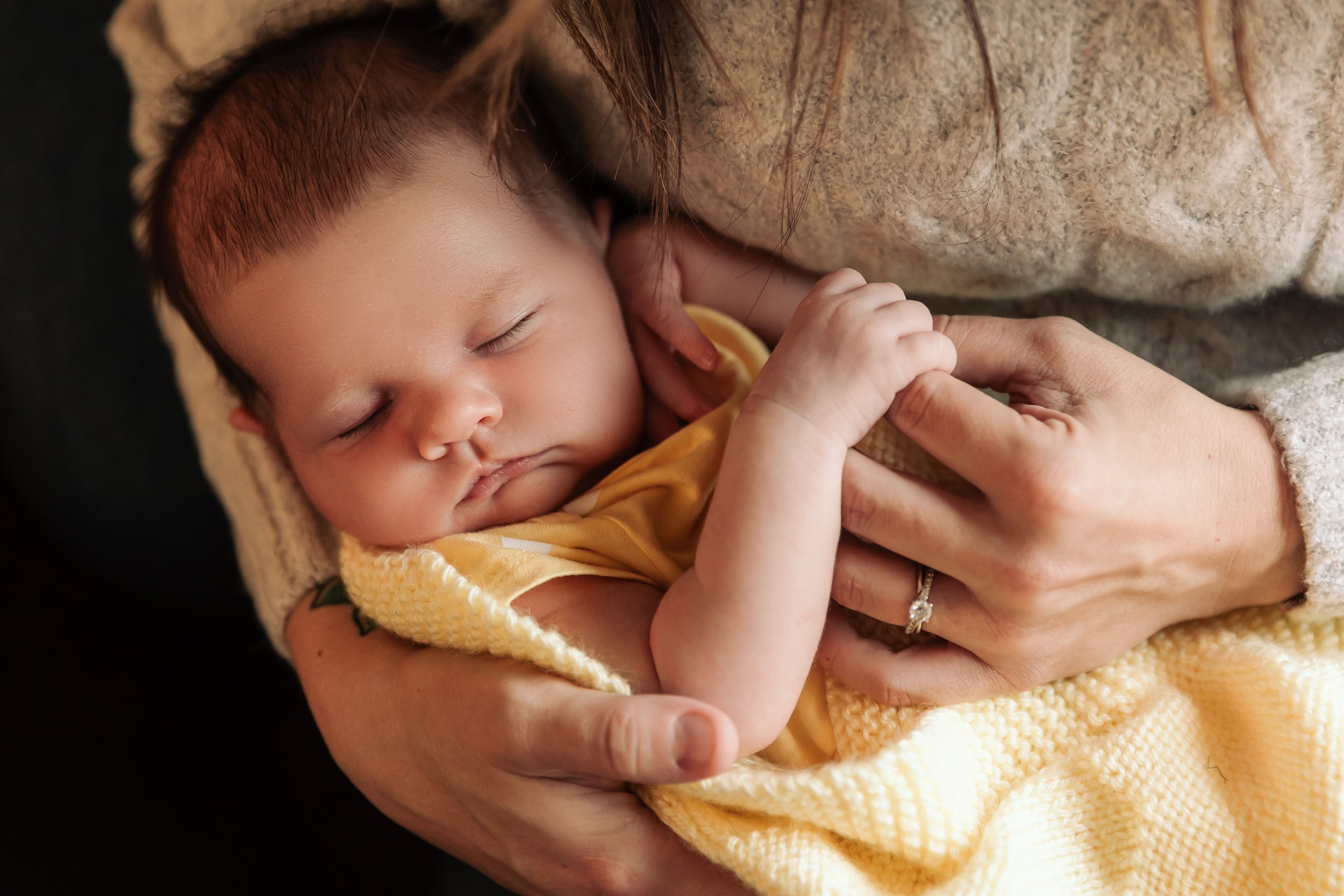 Sleeping baby wrapped in a yellow blanket held by an adult.