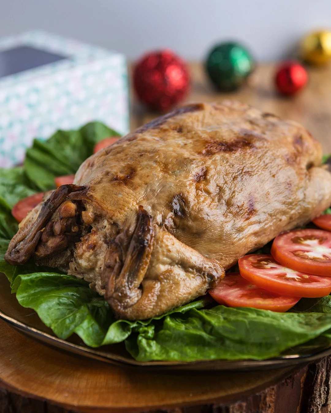 Baked whole chicken on a platter with lettuce and tomato slices, decorated with colorful Christmas ornaments in the background.