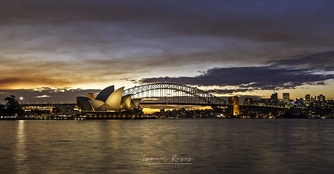 Sunset over Sydney Harbour showing the Sydney Opera House, Harbour Bridge, and city skyline.