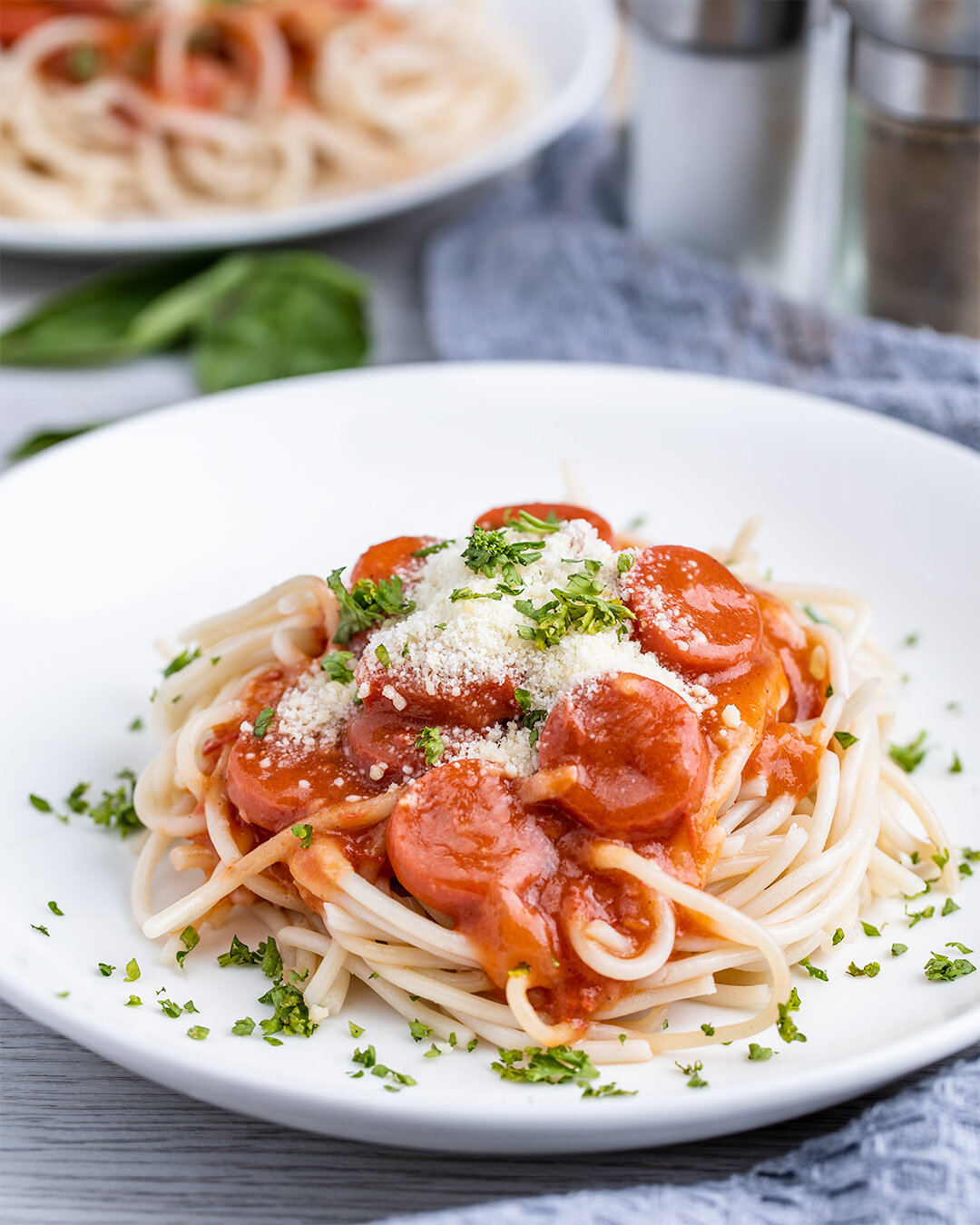 A plate of spaghetti with tomato sauce, cherry tomatoes, grated cheese, and chopped parsley for garnish.