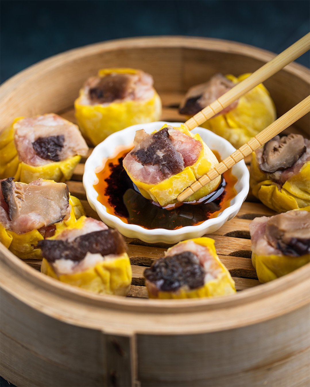 Dim sum with siu mai dumplings in a bamboo steamer, served with soy sauce.