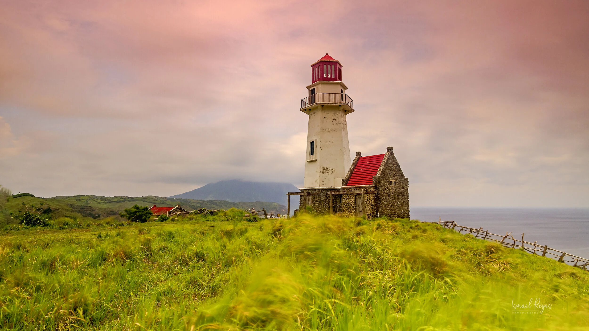 Lighthouse on grassy coastline with cloudy sky and ocean in the background.