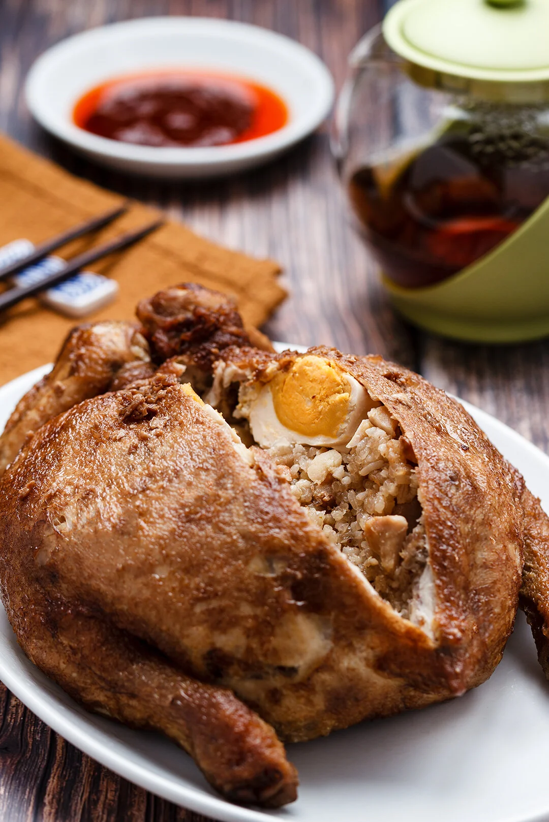 Roast chicken stuffed with rice, chopped chicken, and a boiled egg, served on a white plate with dipping sauces in the background.