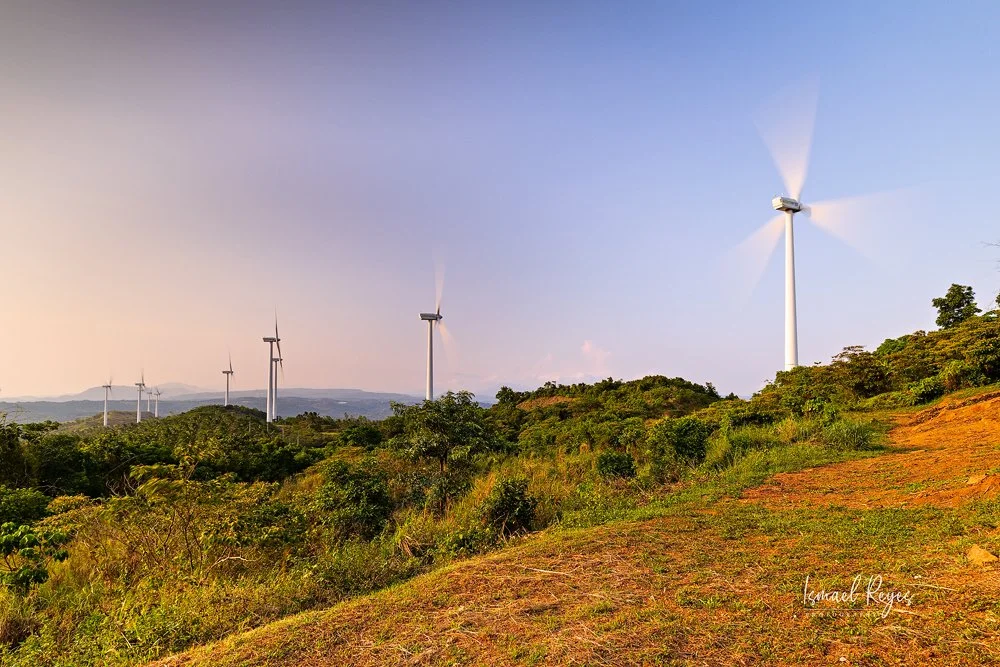 Scenic view of a green landscape with several wind turbines on a hill under a clear sky, early morning or late afternoon light.