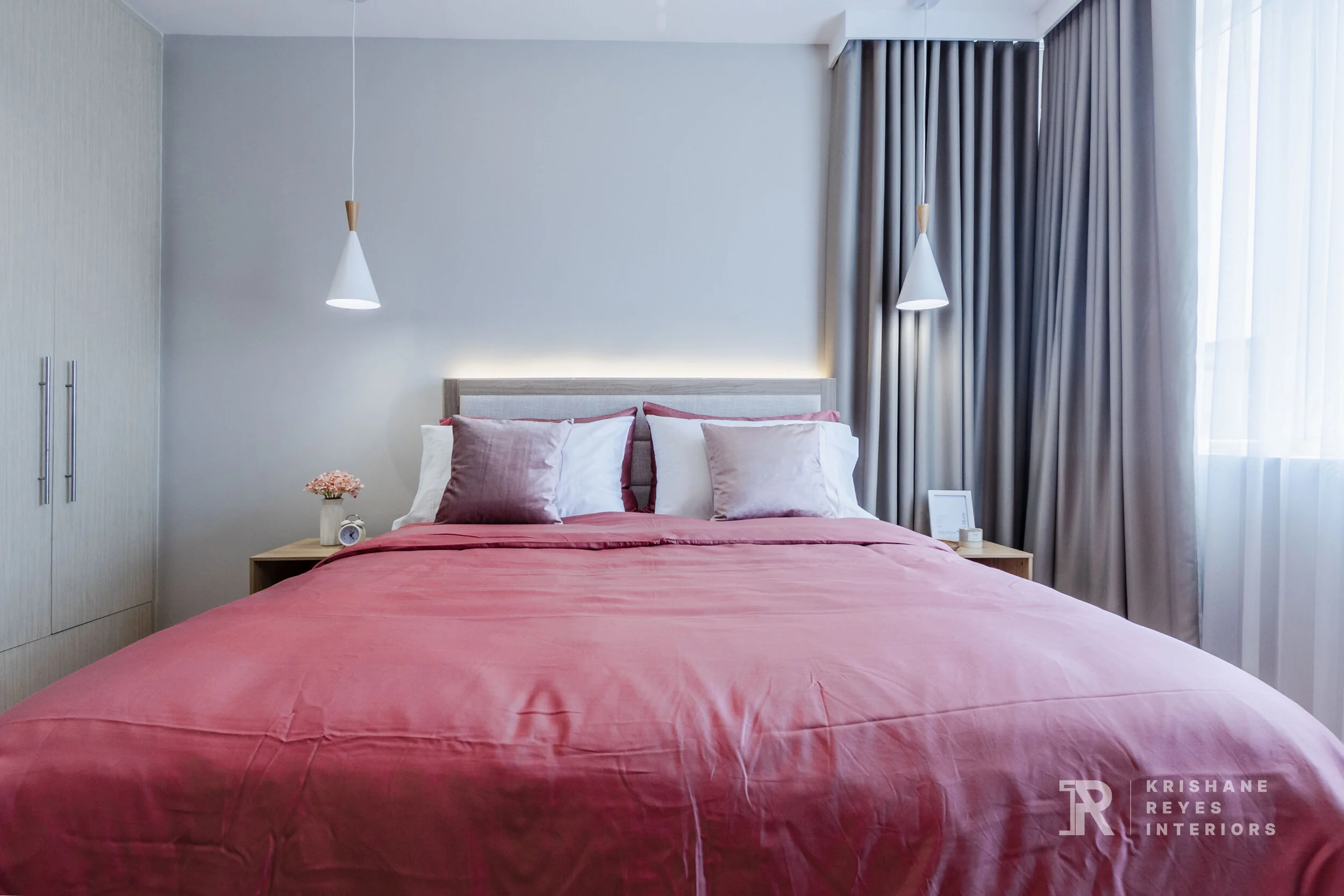 Modern bedroom with a large bed covered in pink bedding, pink and white pillows, bedside tables with decor, and gray curtains on the window