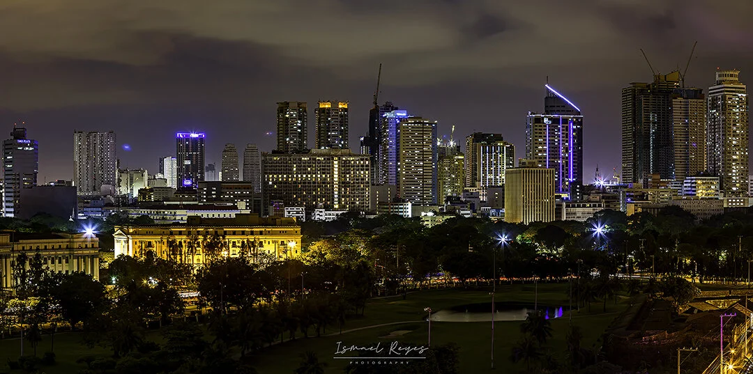 City skyline at night with tall illuminated buildings and a park in the foreground