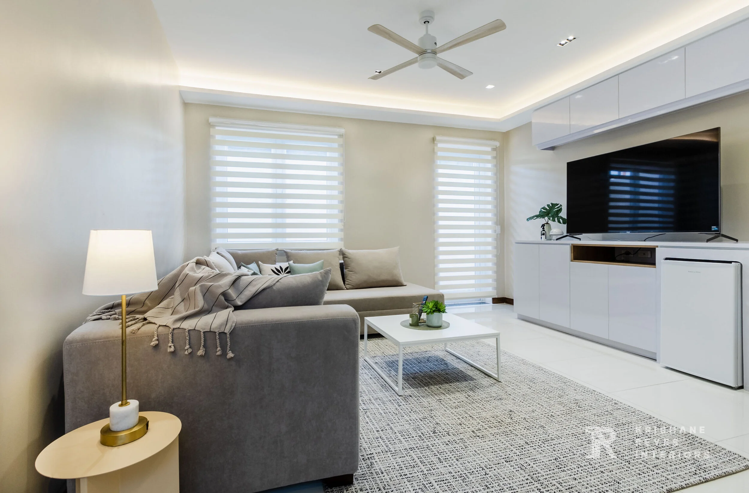 Modern living room with a gray sofa, white coffee table, large television, white built-in cabinetry, and large windows with white blinds