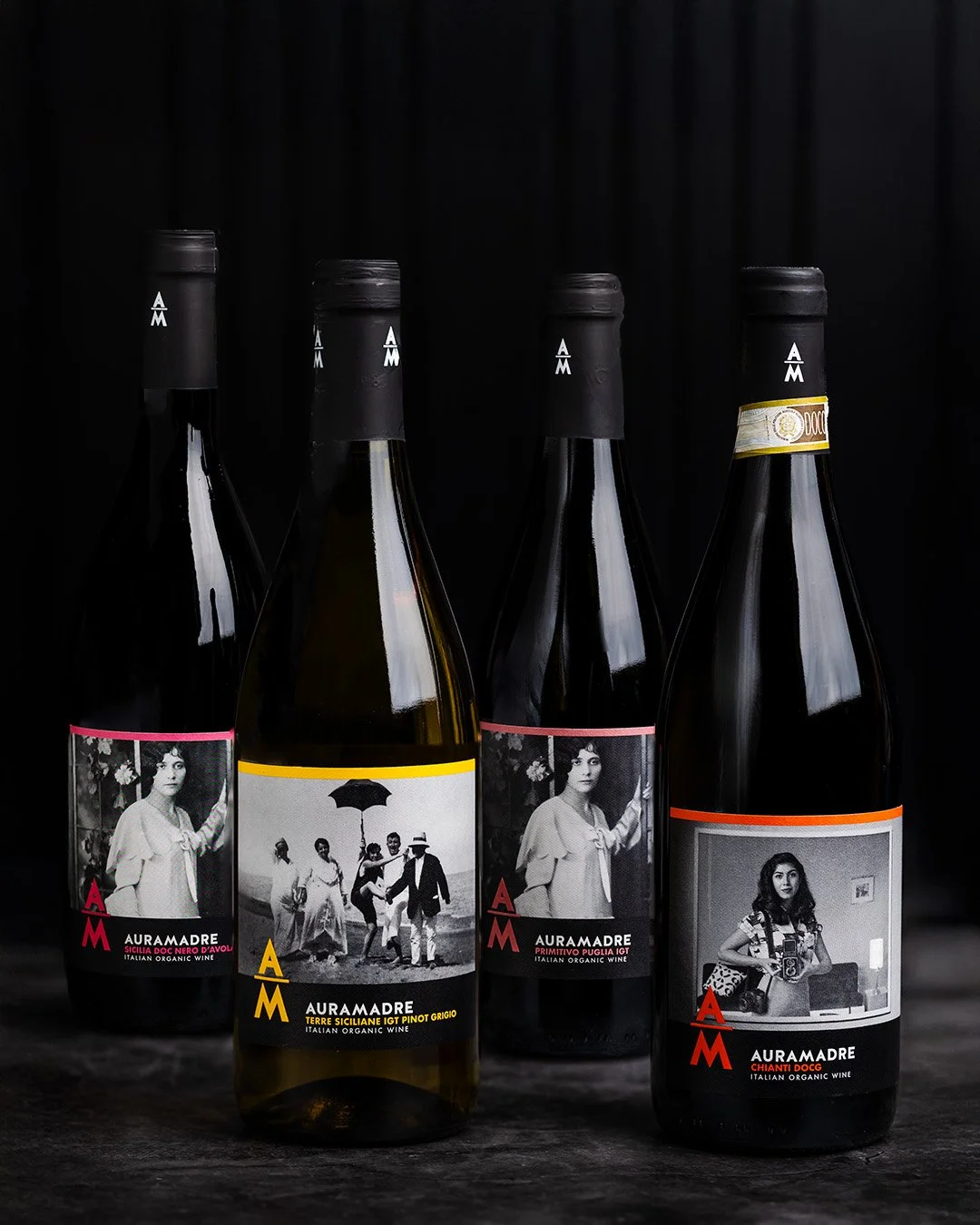 Four bottles of organic Italian wine with black labels and artistic black-and-white photographs, arranged on a dark surface against a black background.