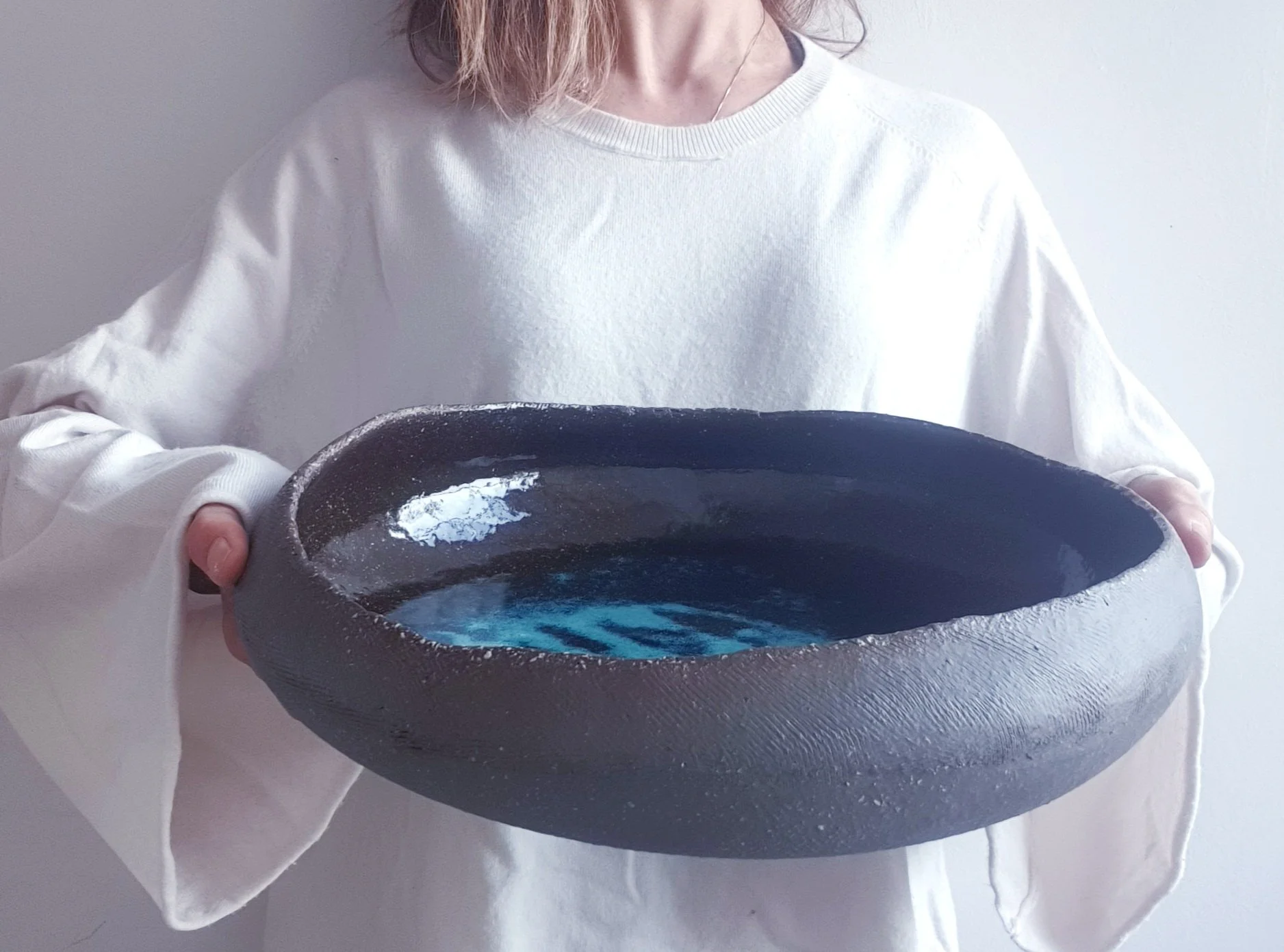 Persona che tiene una ciotola  in gres grigio con smalto blu, indossa una maglietta bianca e si trova davanti a uno sfondo bianco.