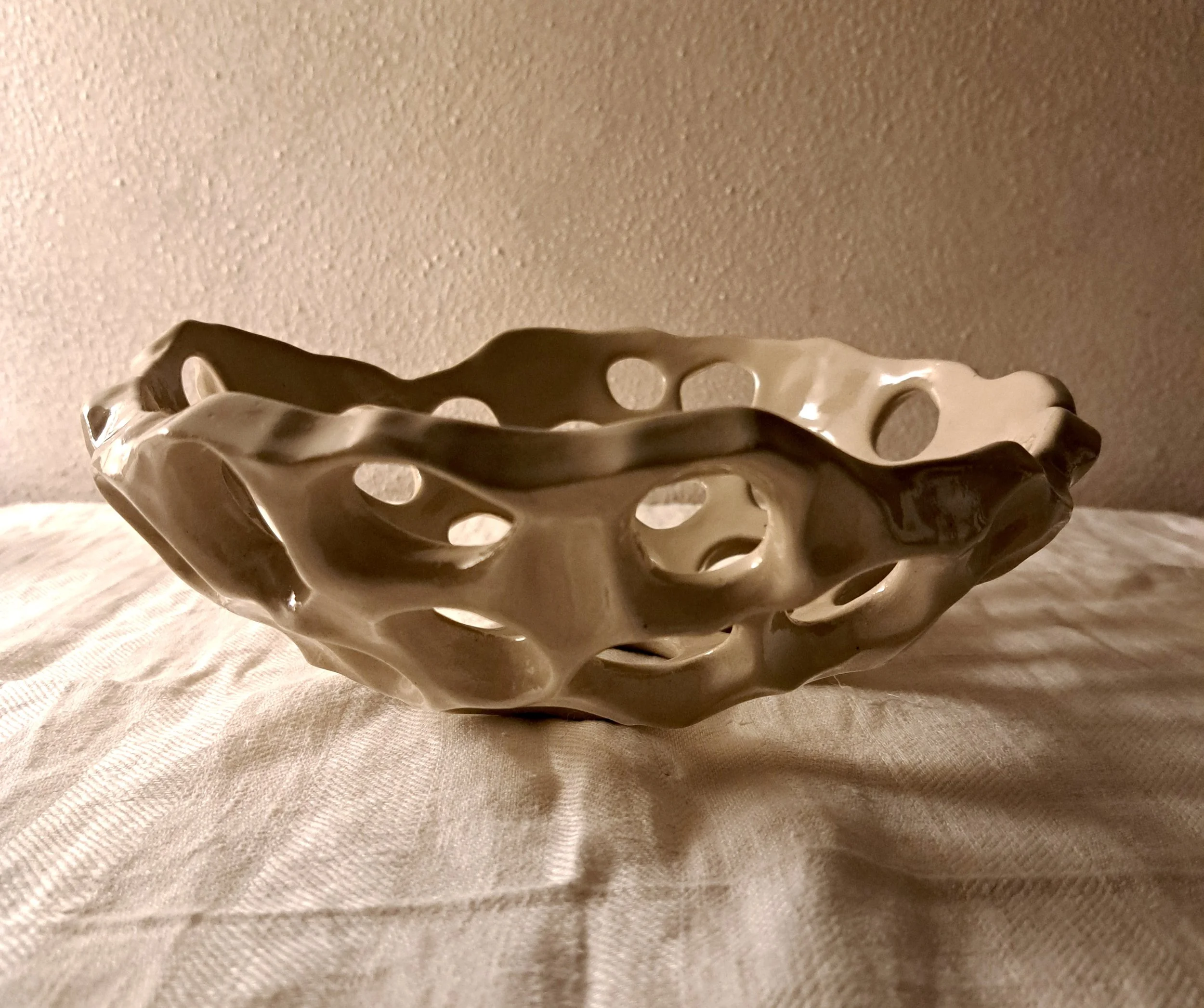 Un oggetto di ceramica con fori arrotondati, sembra una struttura decorativa o funzionale, posizionato su un tessuto bianco.