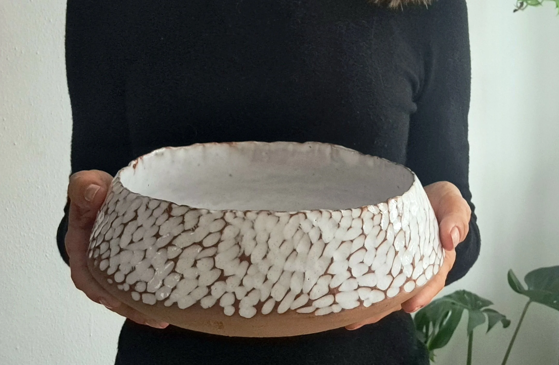 Persona che tiene in mano una ciotola di ceramica bianca con motivo intrecciato.