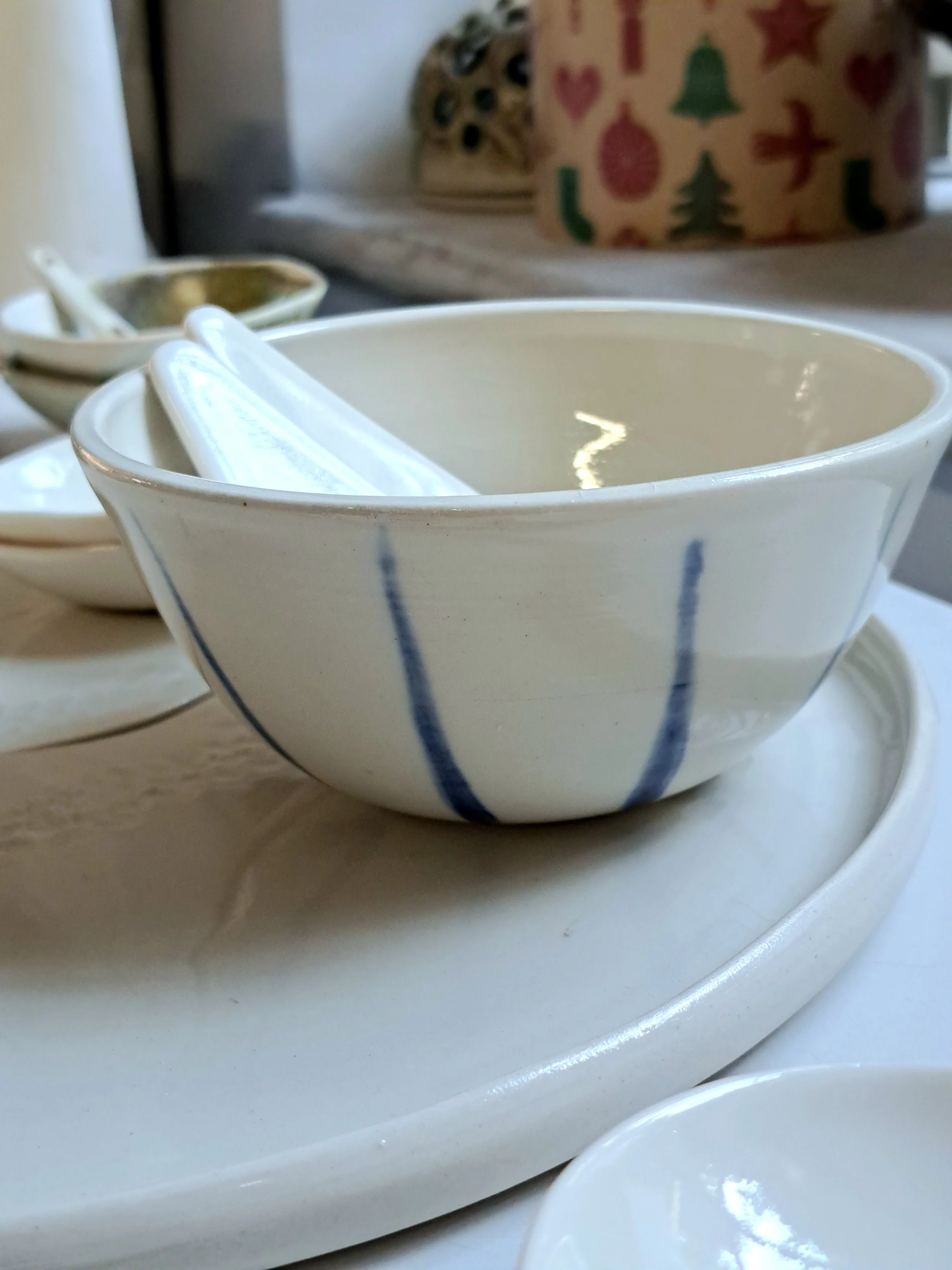 Alcuni piatti e ciotole di ceramica bianca con decorazioni blu, una di esse contiene bacchette di legno, tutte posizionate su un piano bianco.