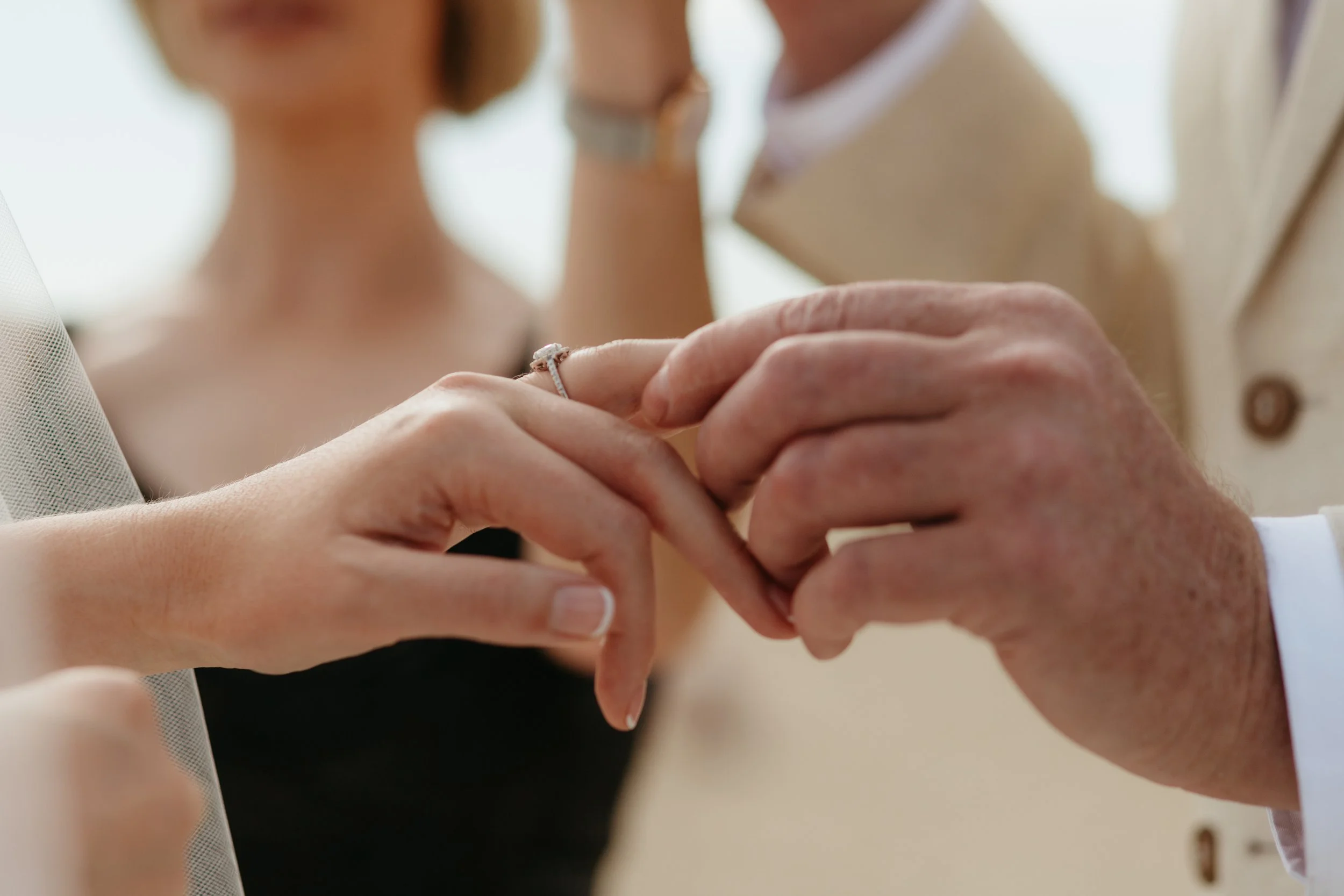 A close-up of a woman's hand with a ring on her finger, as she holds a man's hand during a wedding ceremony.