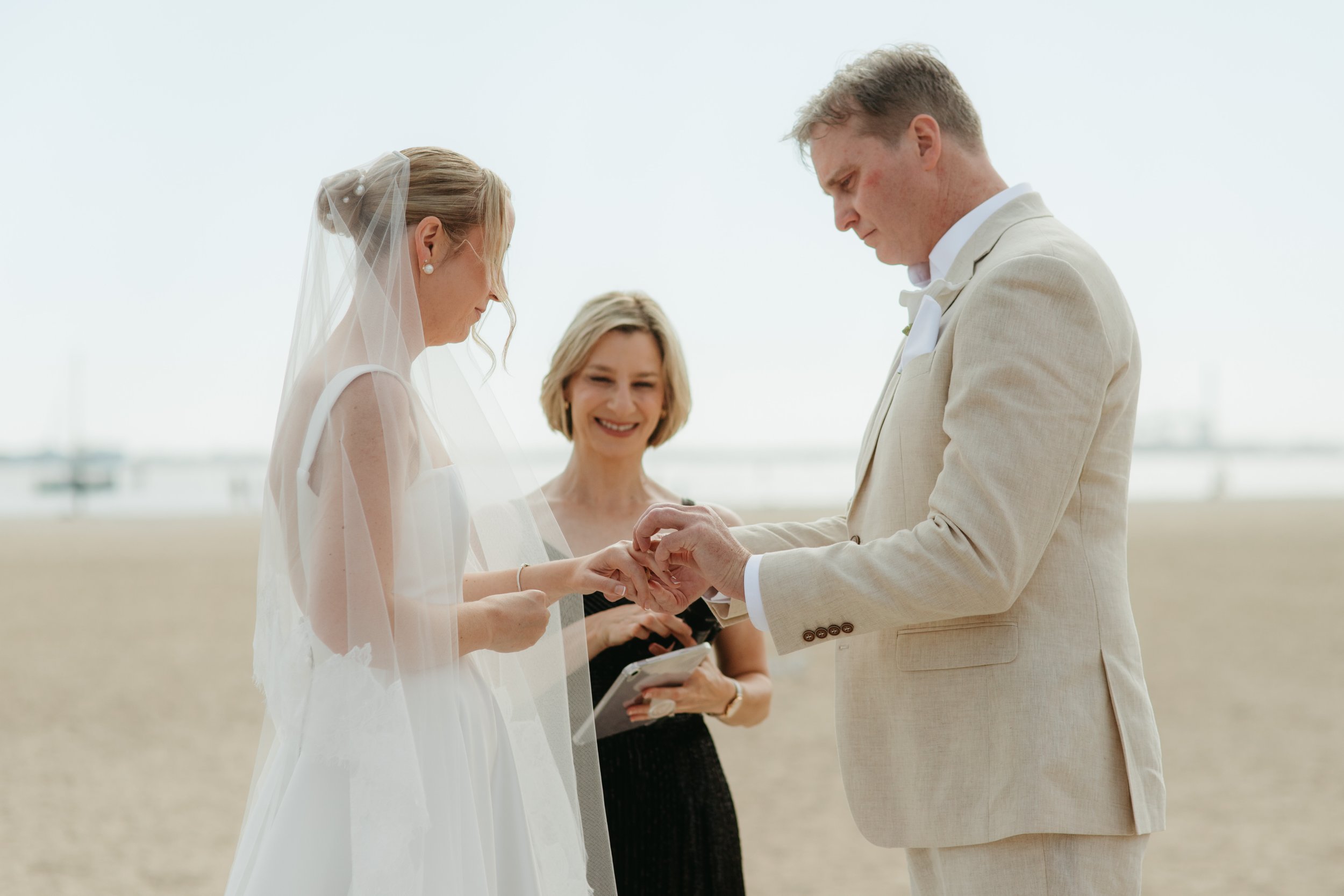 A couple getting married outdoors with an officiant present, during daytime over a cloudy sky.