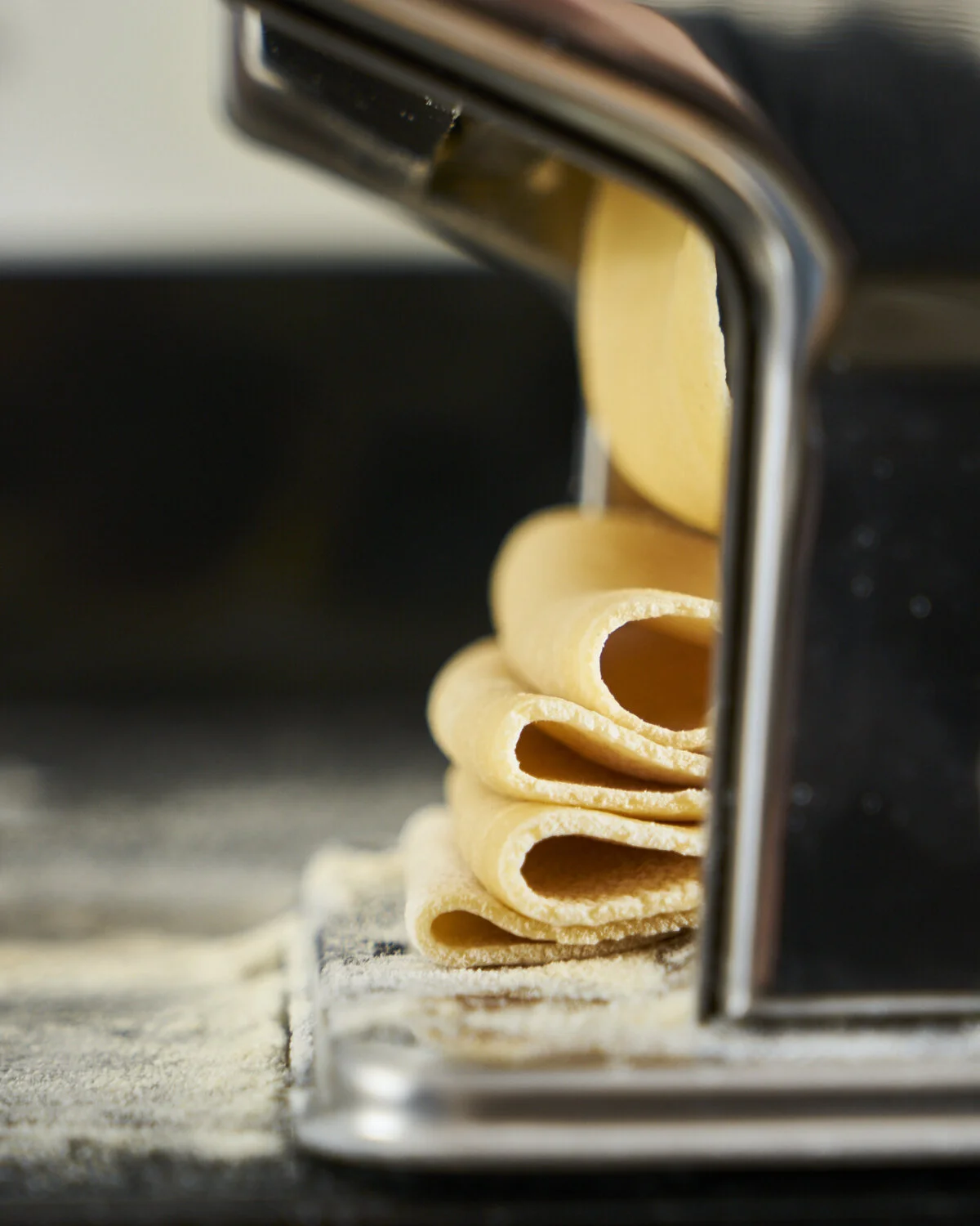 Close-up of uncooked pasta being sliced by a pasta cutter on a floured surface.