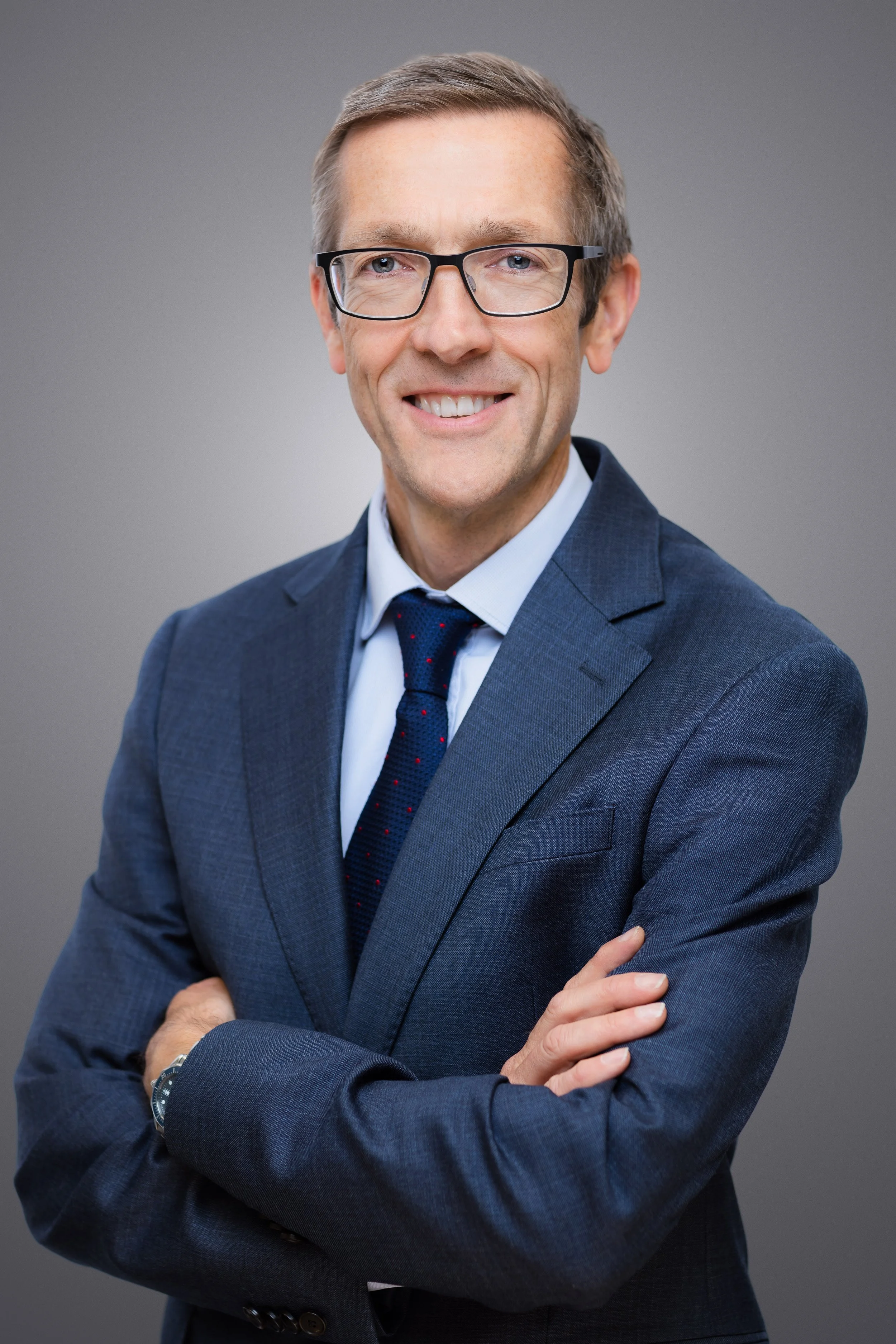 business headshot of a man smiling looking at the camera he is wearing glasses